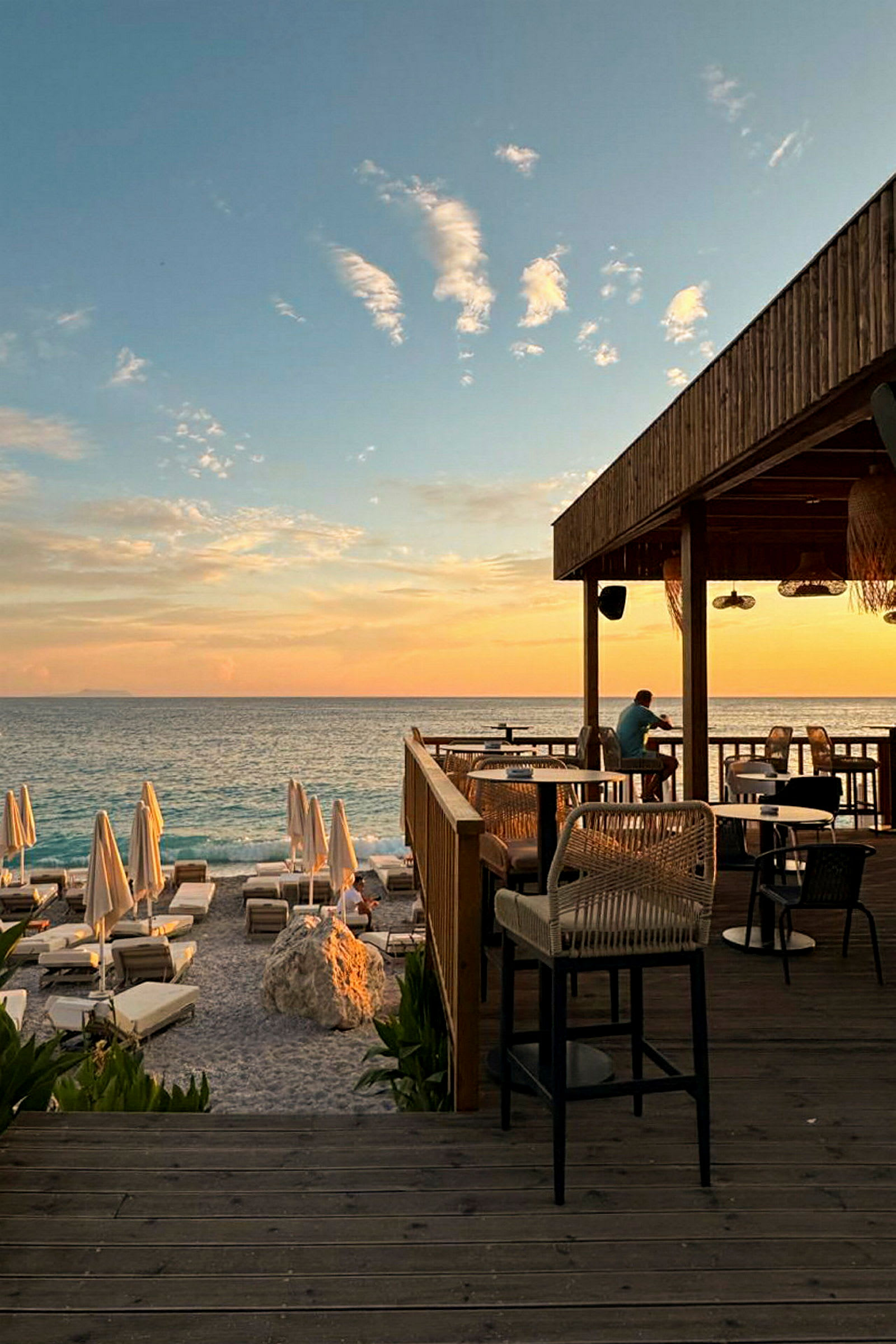 En solnedgang ved havet med en restaurantterrasse og solsenge på stranden. (AI-genereret tekst)