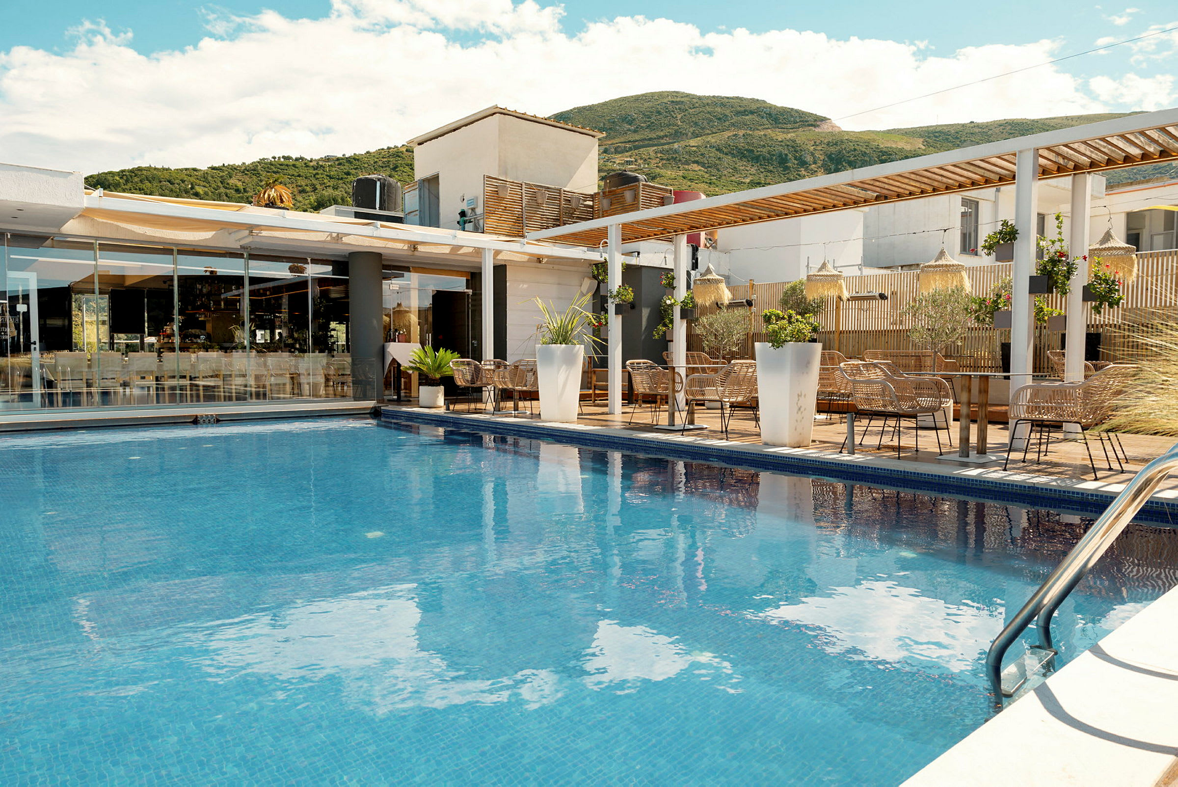 En udendørs pool foran et moderne hotel med terrasse og haveudsmykning. (AI-genereret tekst)