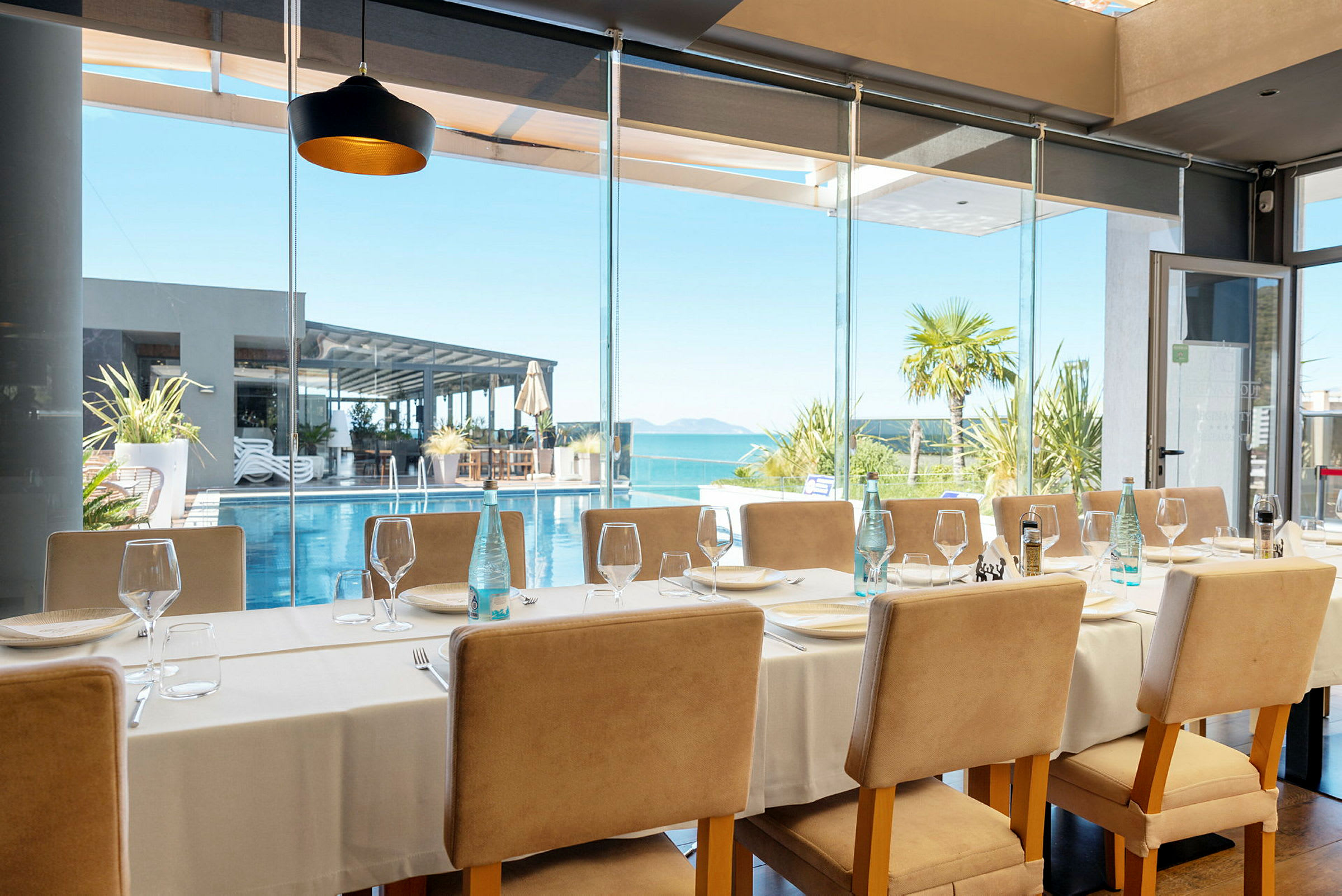 Restaurant med opstillet bord og udsigt til pool og hav. (AI-genereret tekst)