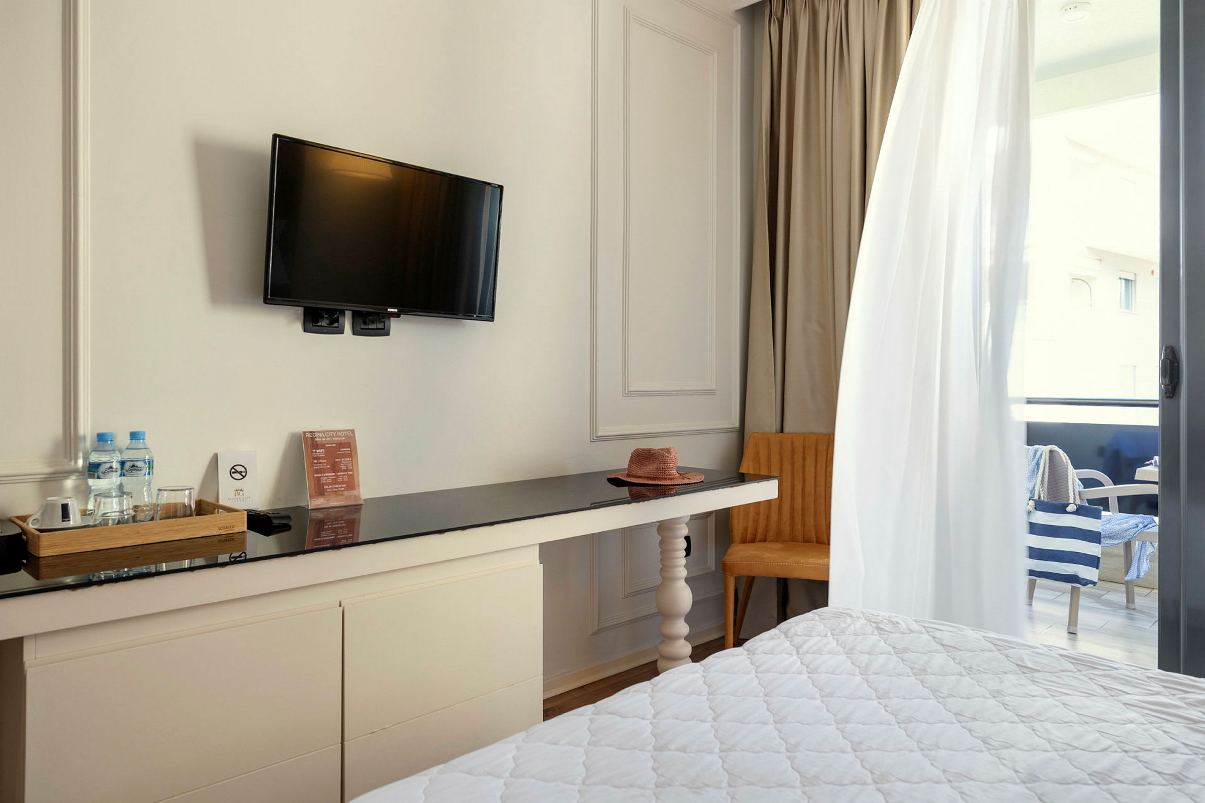 Hotelværelse med tv på væggen, skrivebord, stol og delvist synlig altan. (AI-genereret tekst)