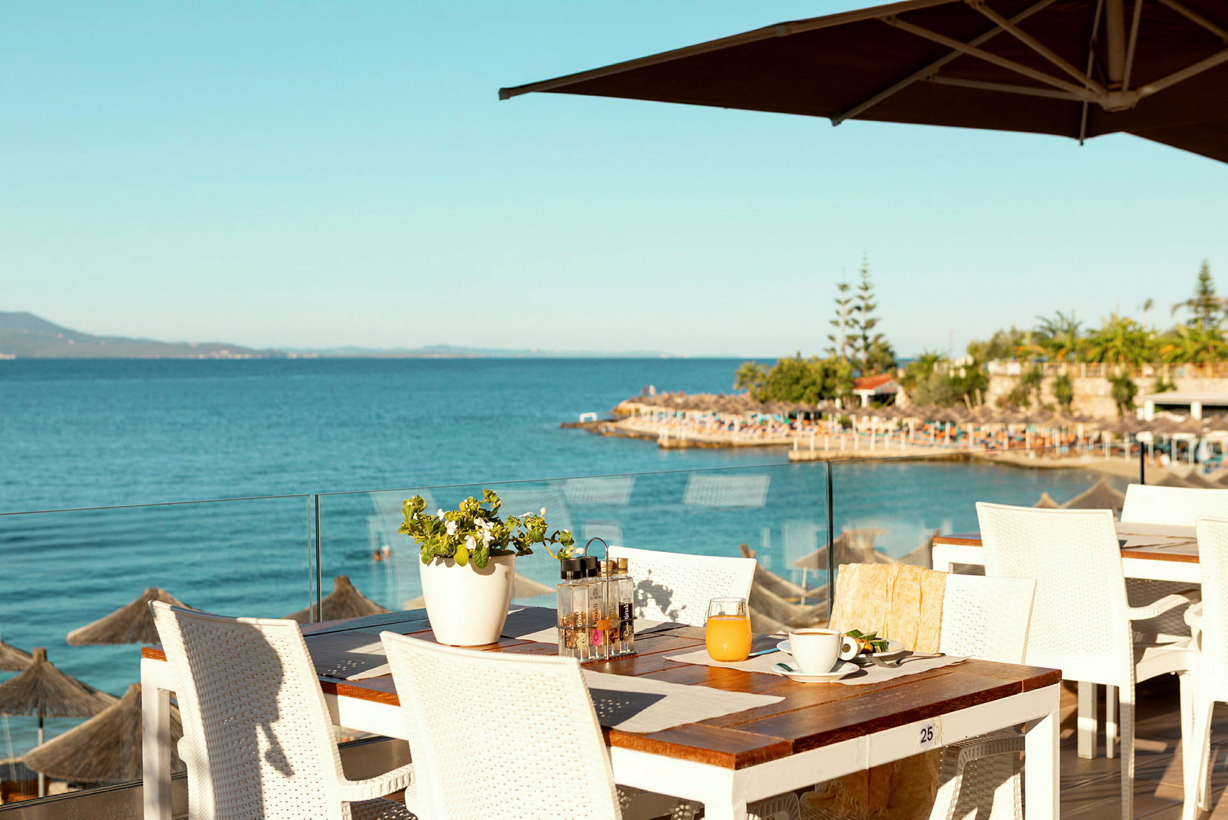 Udsigt over havet fra en restaurantterrasse med hvide borde og stole. (AI-genereret tekst)