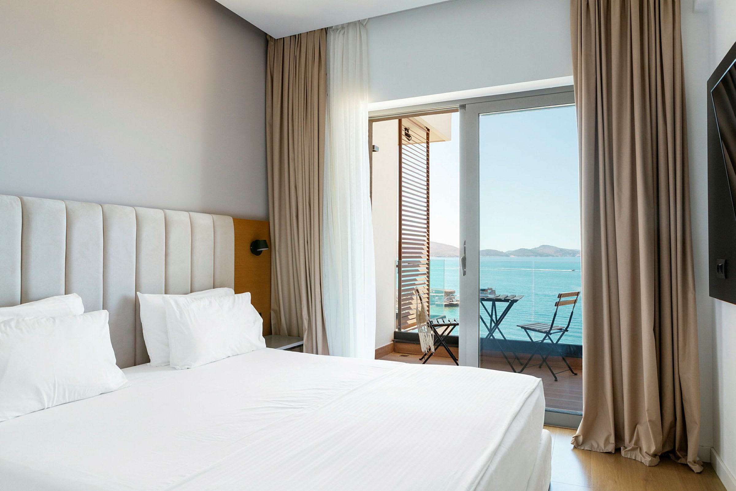 Billede af et hotelværelse med seng og en balkon med udsigt over havet. (AI-genereret tekst)