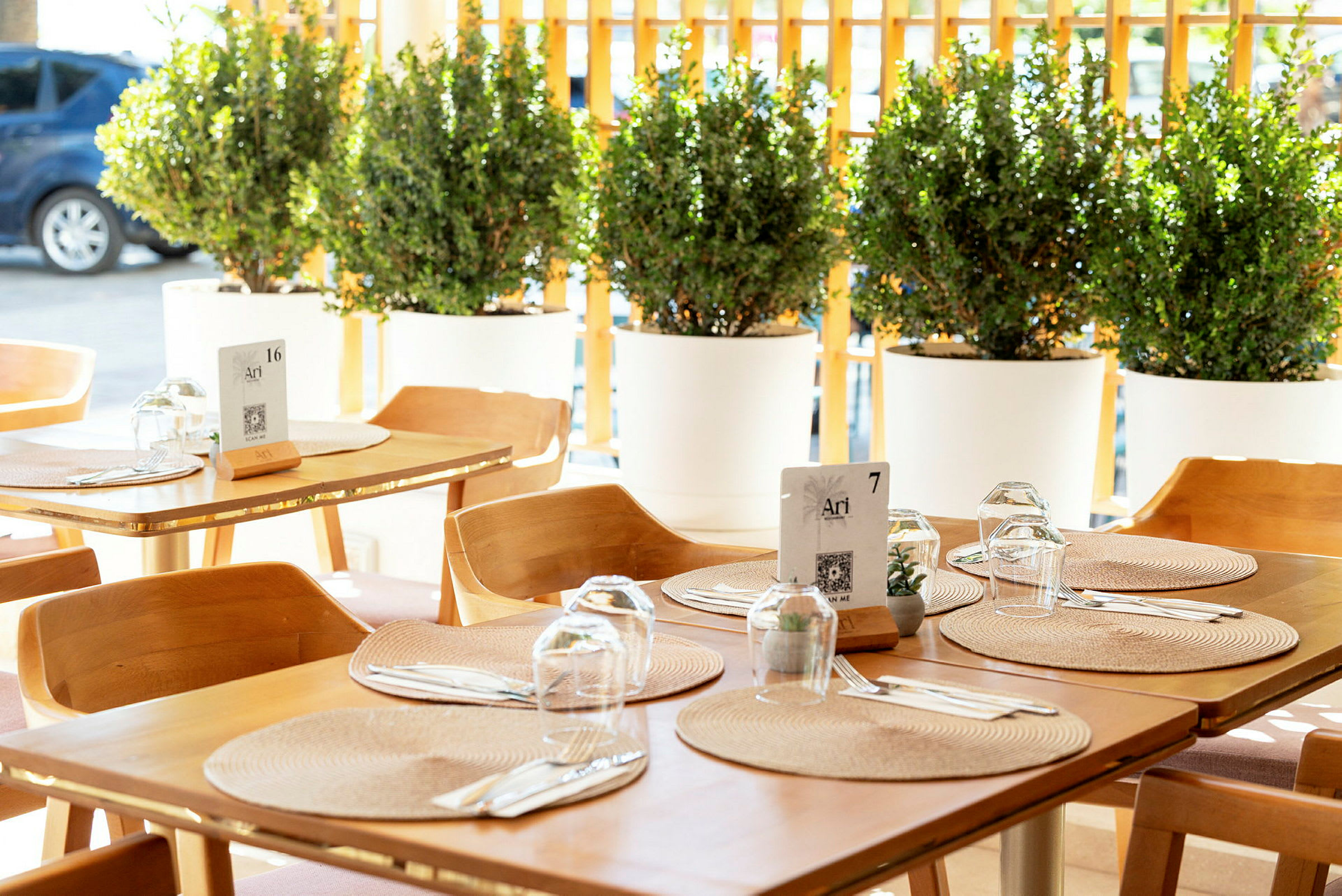 Opdækket bord i restaurant med træstole og runde underlag, omgivet af grønne potteplanter. (AI-genereret tekst)