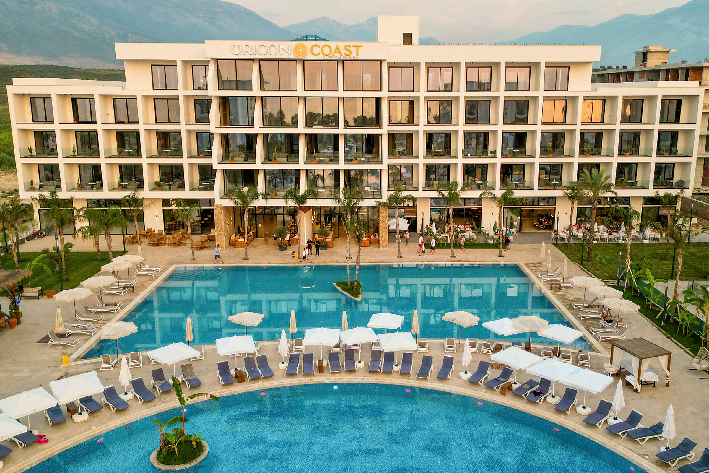 Et hotel med en stor udendørs pool og liggestole omgivet af grønne områder. (AI-genereret tekst)