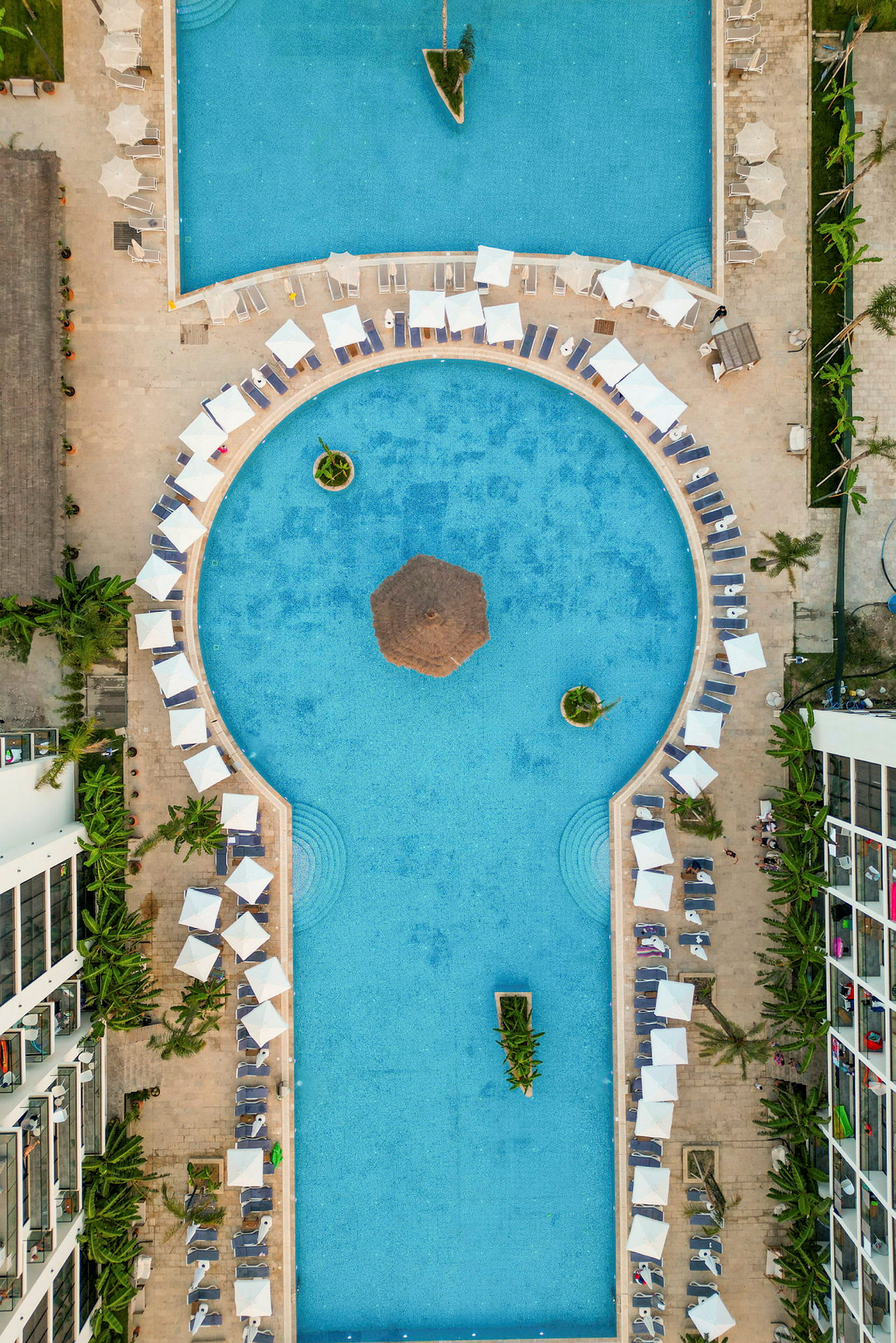 Luftfoto af en pool med liggestole og parasoller rundt om. (AI-genereret tekst)