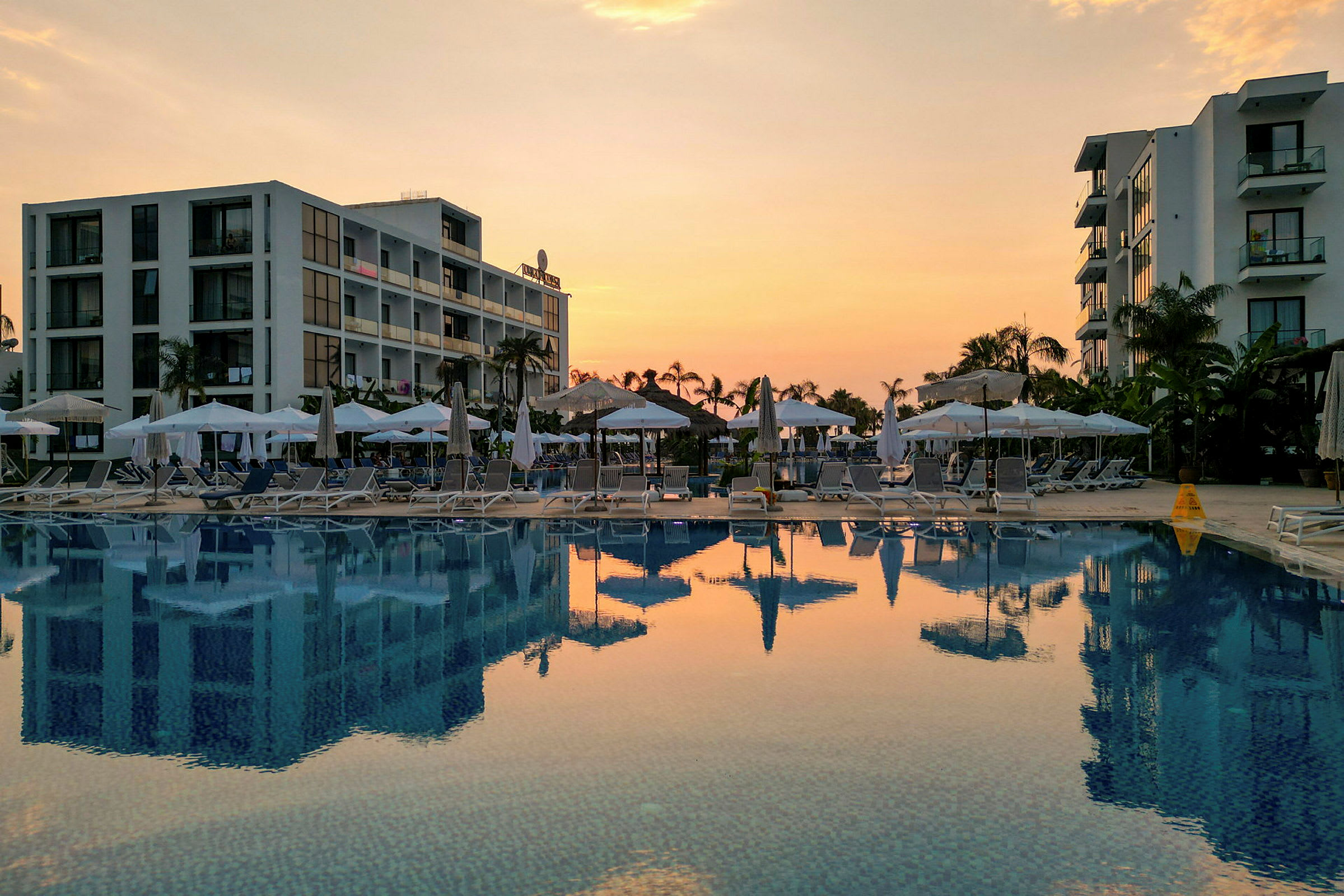 Hotelbygninger og en pool ved solnedgang. (AI-genereret tekst)