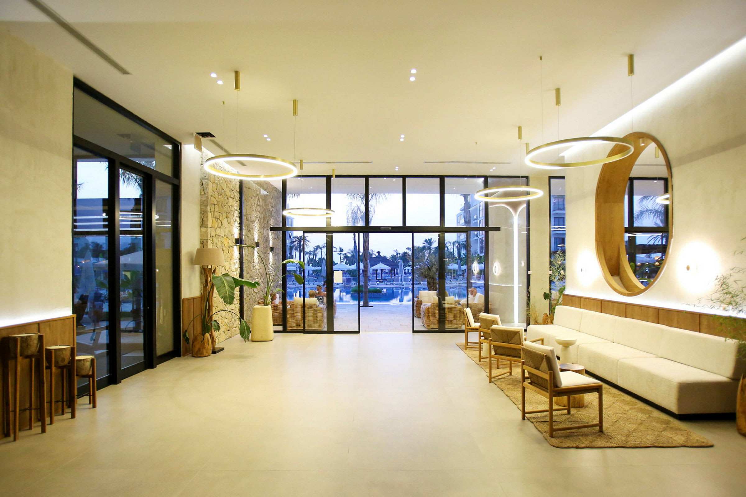 Et moderne hotellobbyområde med behagelige siddepladser, stilfulde lamper og store glasdøre, der fører til et poolområde. (AI-genereret tekst)