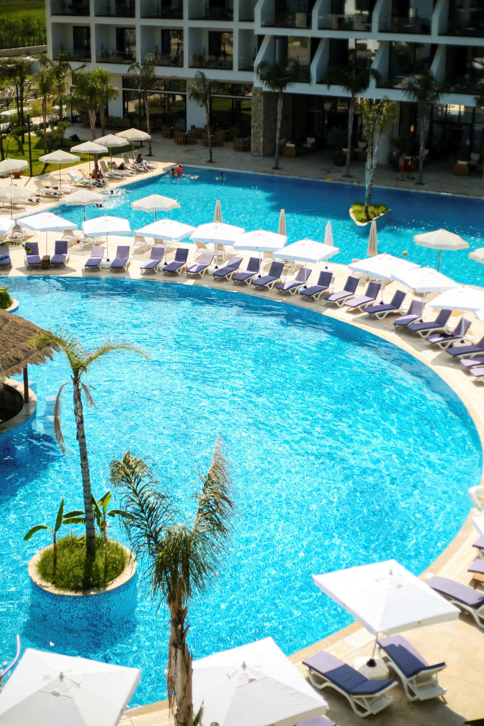 En swimmingpool med liggestole og parasoller ved et hotel. (AI-genereret tekst)