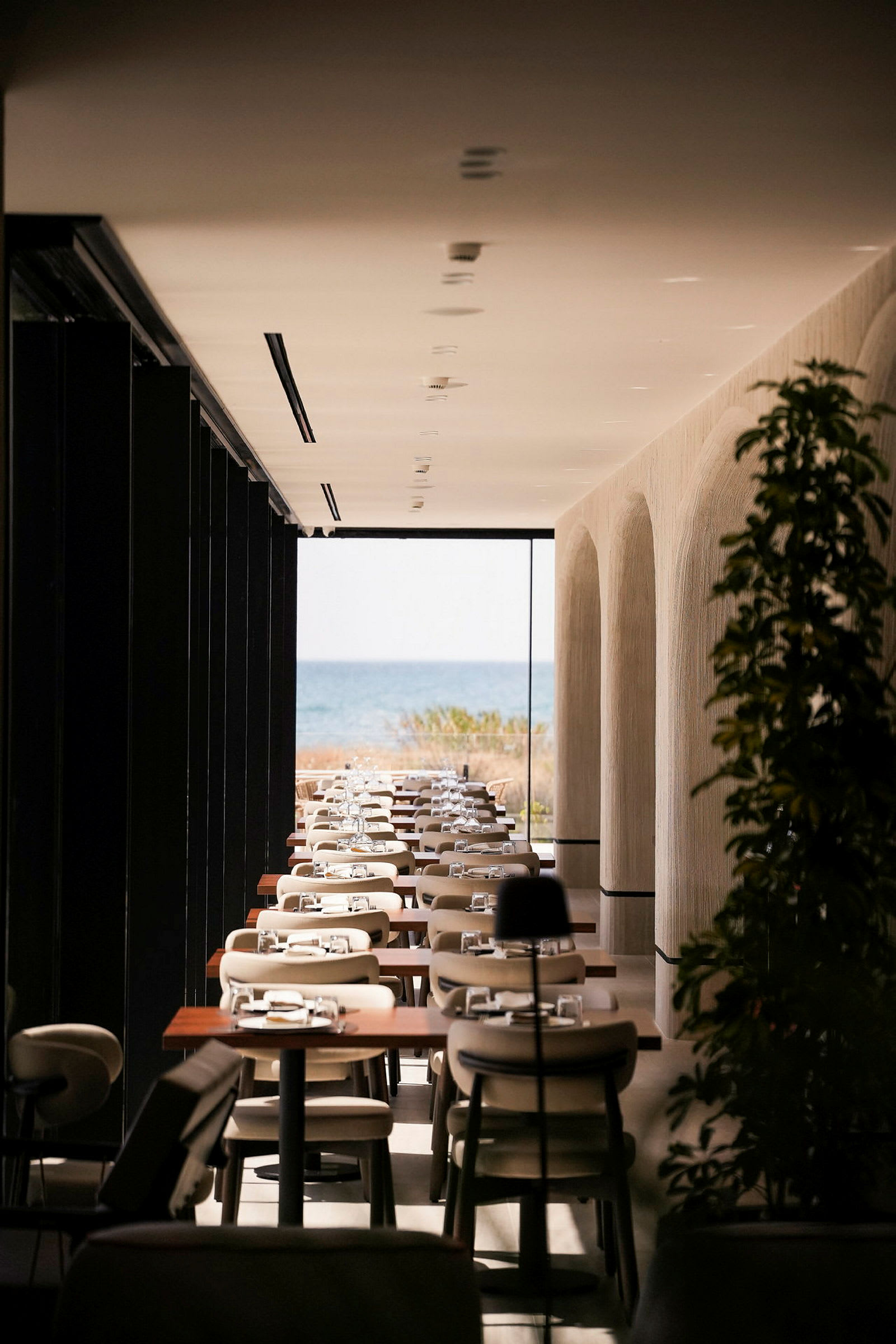 Et moderne indrettet restaurantområde med dækkede borde og udsigt over havet i baggrunden. (AI-genereret tekst)