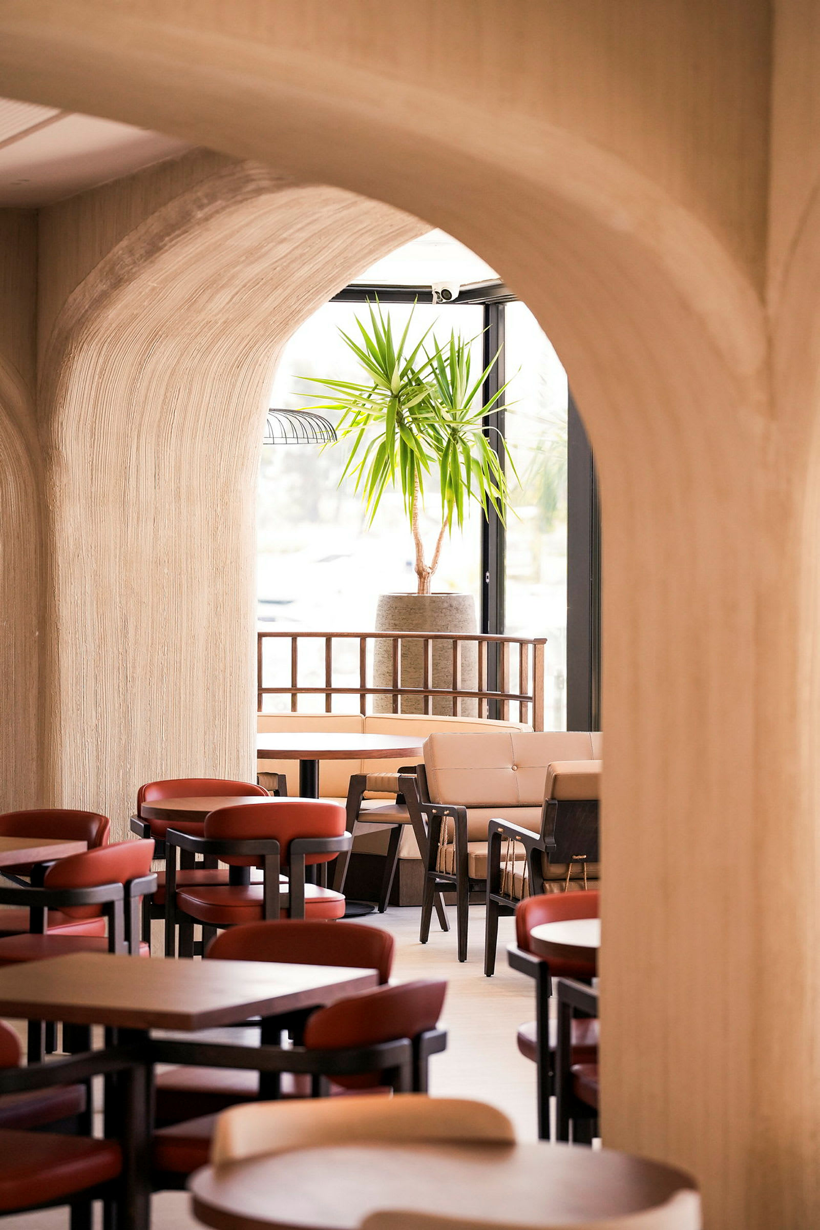 Et interiørbillede af en restaurant eller café med bueformede indgange, borde og stole samt en grøn plante i baggrunden. (AI-genereret tekst)