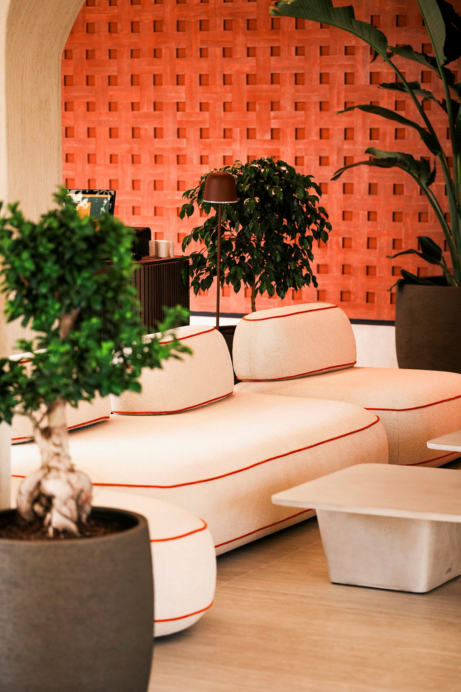 En moderne dagligstue med en beige sofa med orange kant, et sofabord og grønne planter foran en murstensvæg. (AI-genereret tekst)