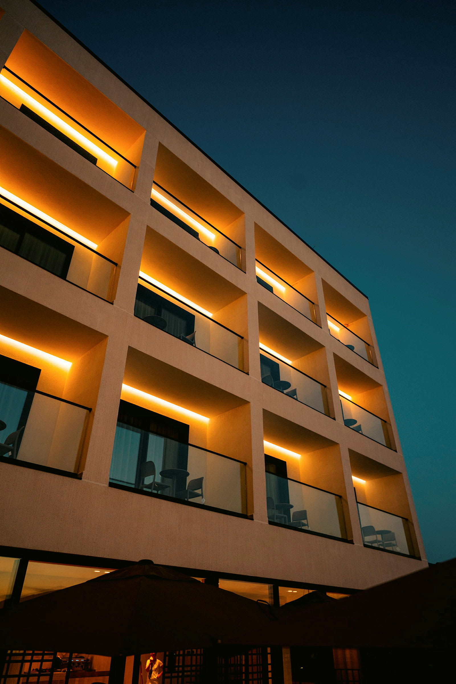 Facade af en moderne bygning med altaner, belyst med varm belysning om aftenen. (AI-genereret tekst)