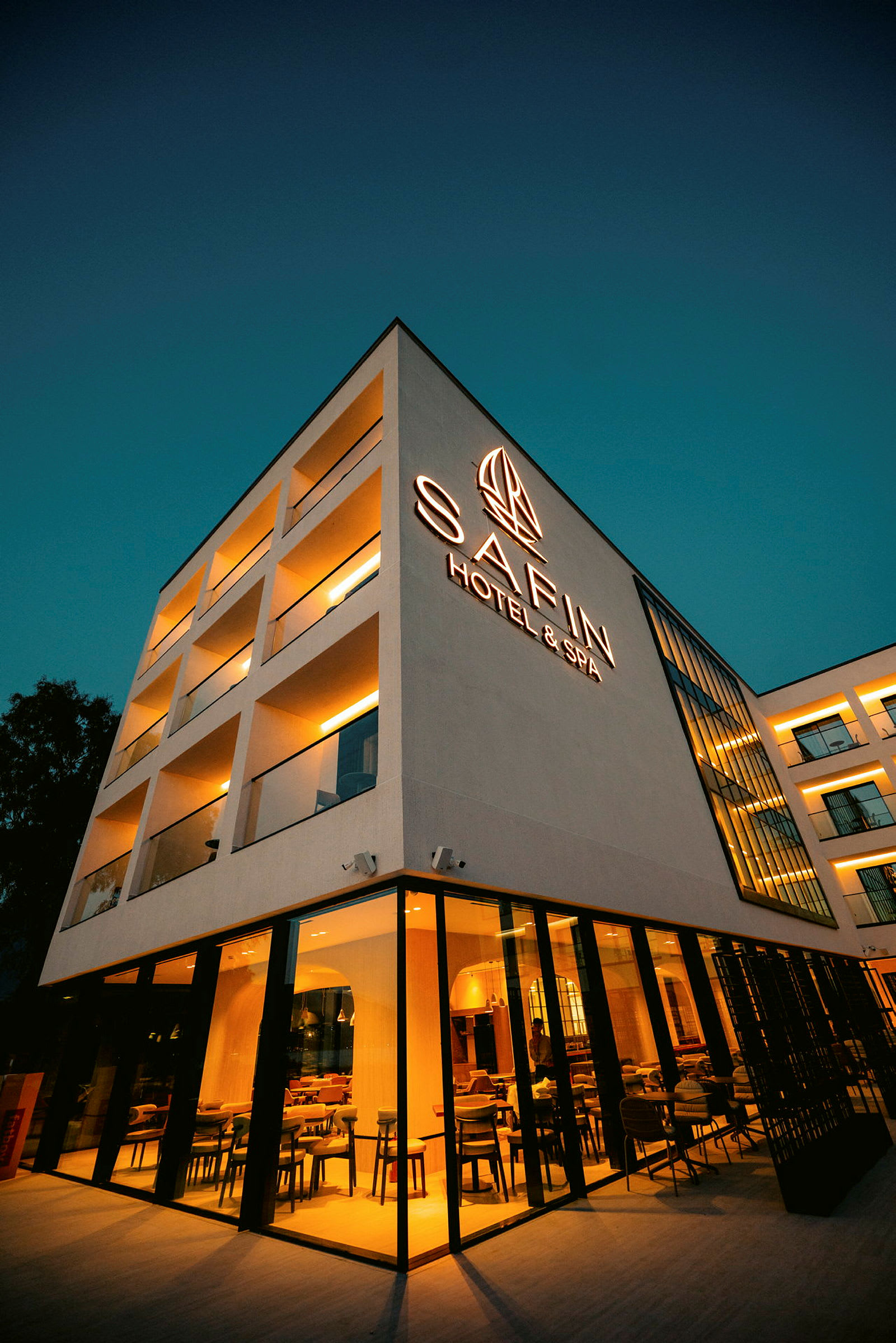 Firkantet bygning oplyst om aftenen, mærket med teksten "Safin Hotel & Spa". (AI-genereret tekst)