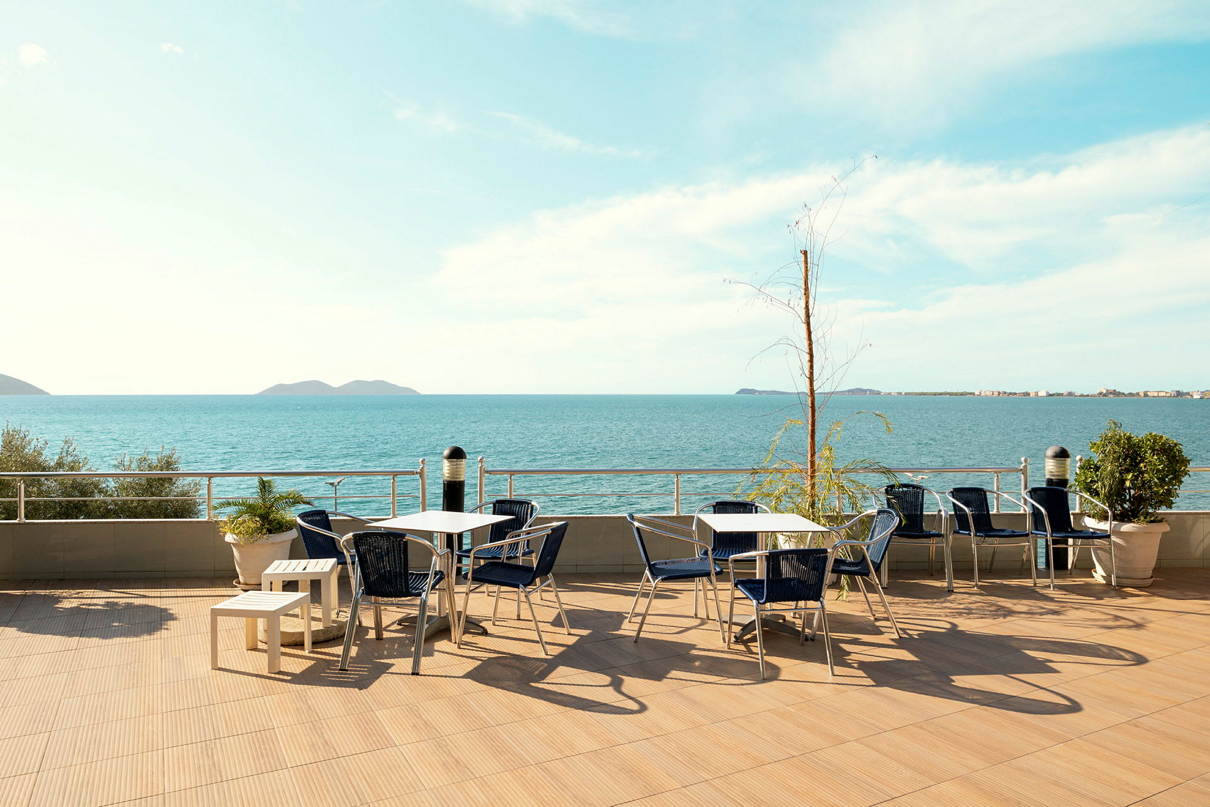 En udendørs terrasse med borde og stole og udsigt over havet. (AI-genereret tekst)