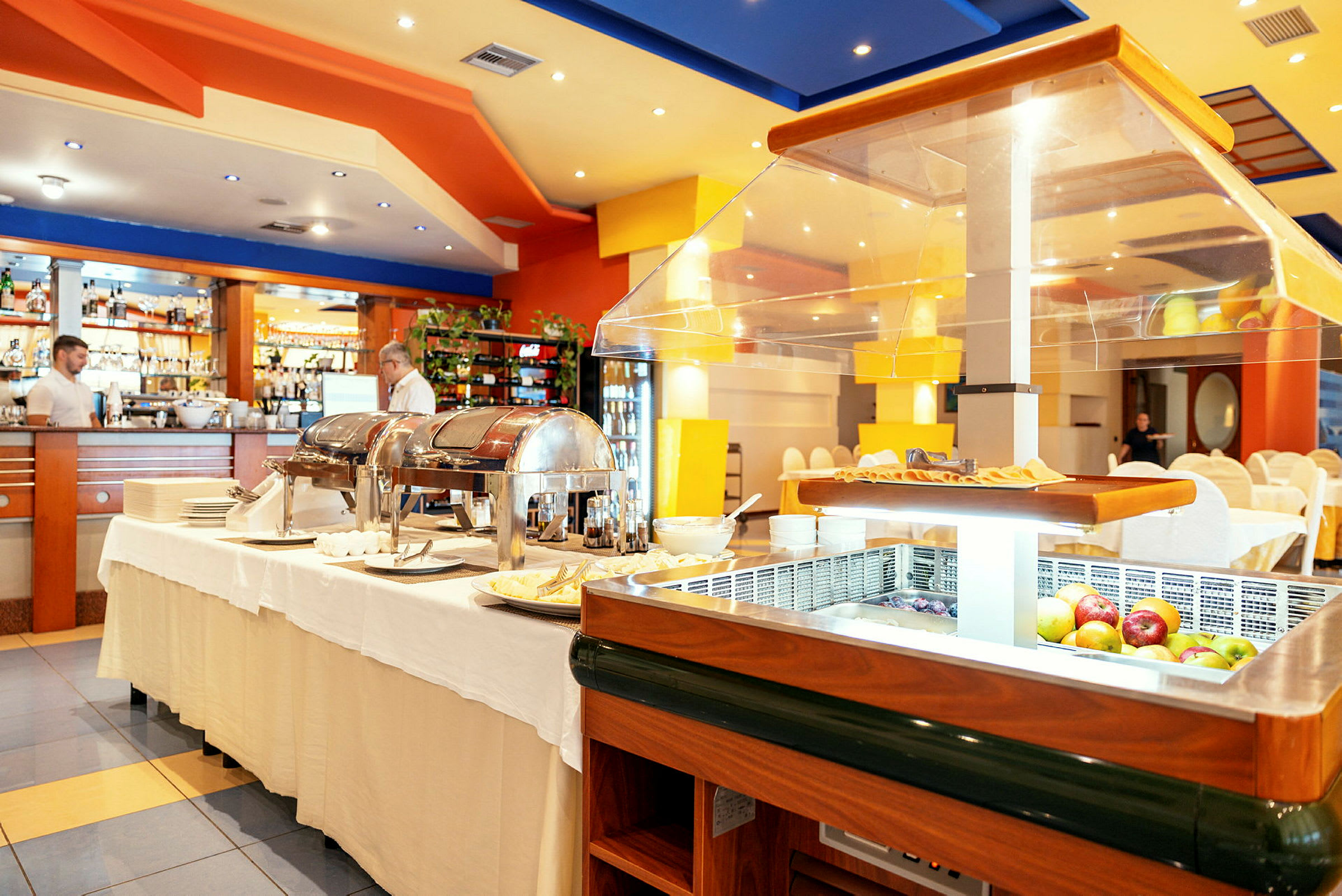 Billede af en restaurantinteriør med buffetudstilling og glasplader på bordene, samt dækkede borde og stole i baggrunden. (AI-genereret tekst)