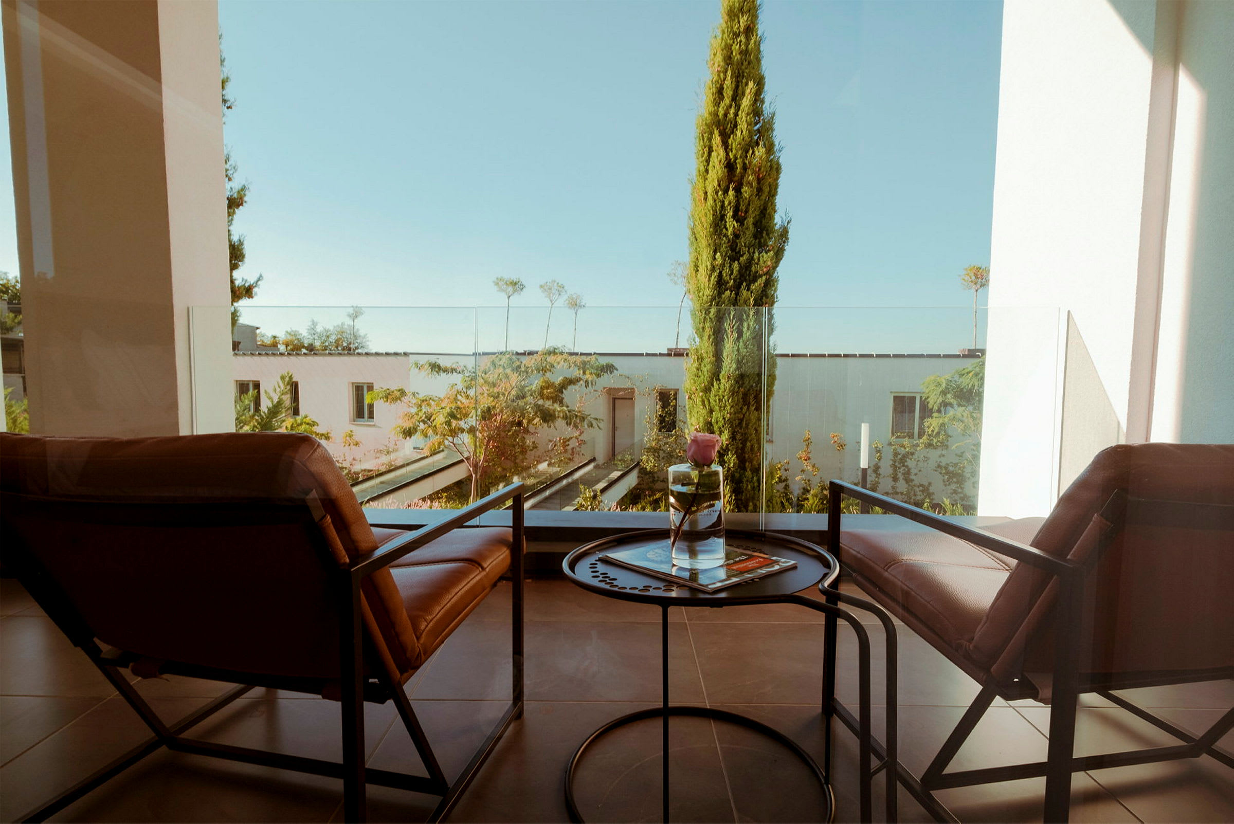 To stole og et lille bord på en balkon med udsigt over en frodig have. (AI-genereret tekst)