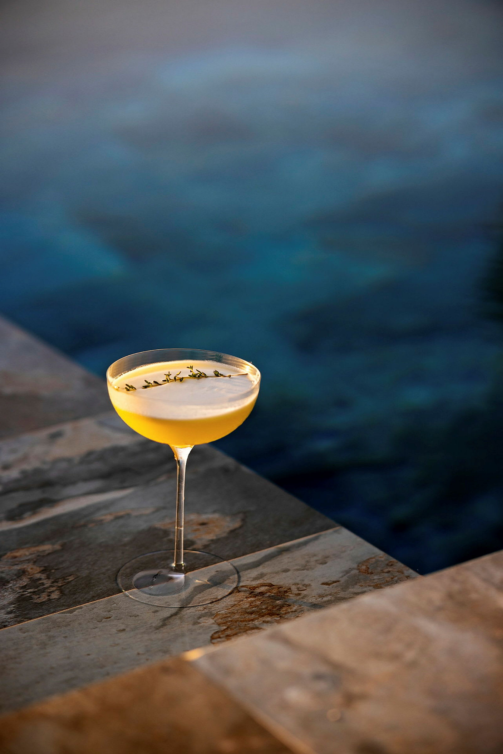 Et glas med en gul drink og pynt står på en stenoverflade ved en pool. (AI-genereret tekst)