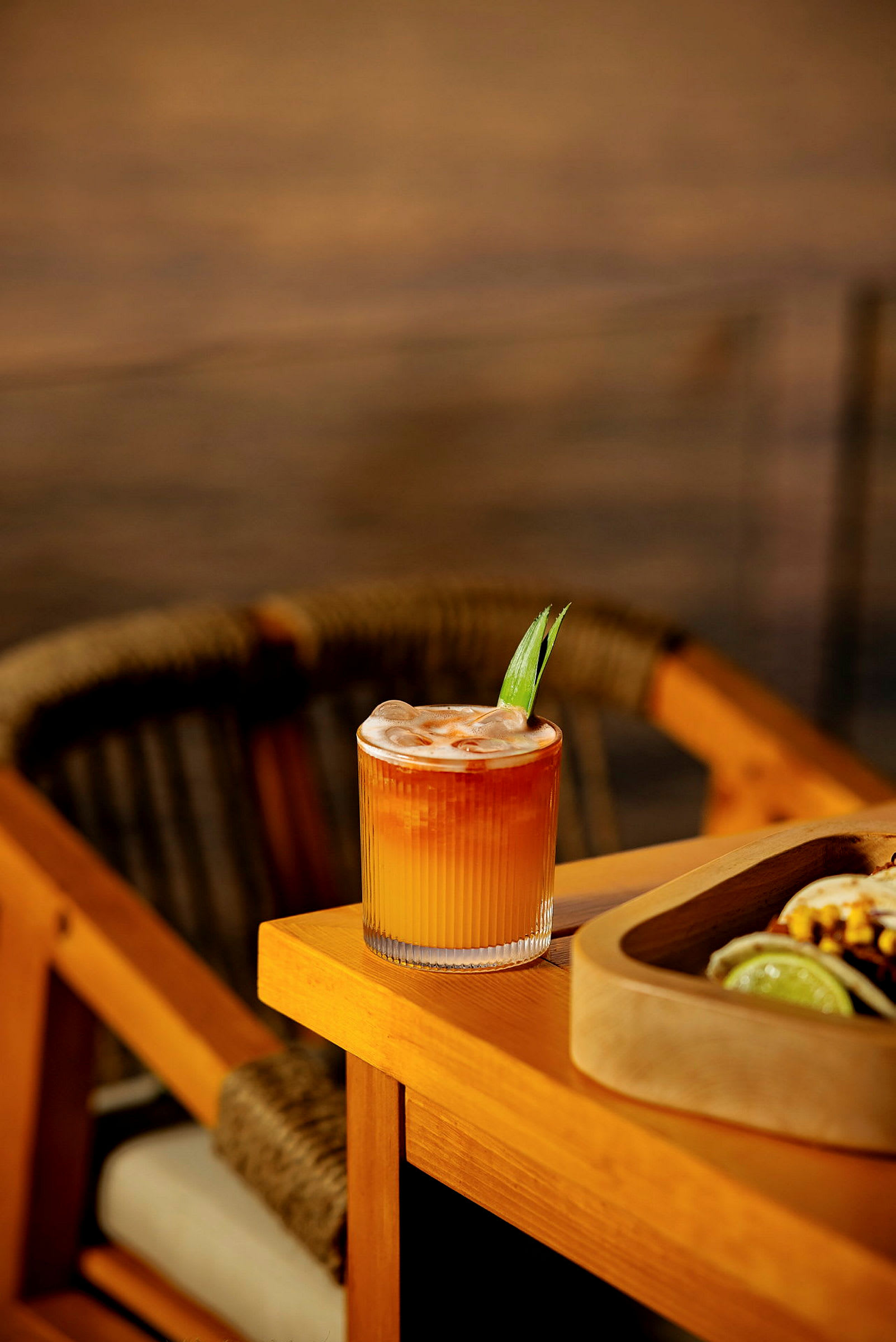 Et glas med en orange drink toppet med is og dekoreret med et blad står på et træbord. (AI-genereret tekst)