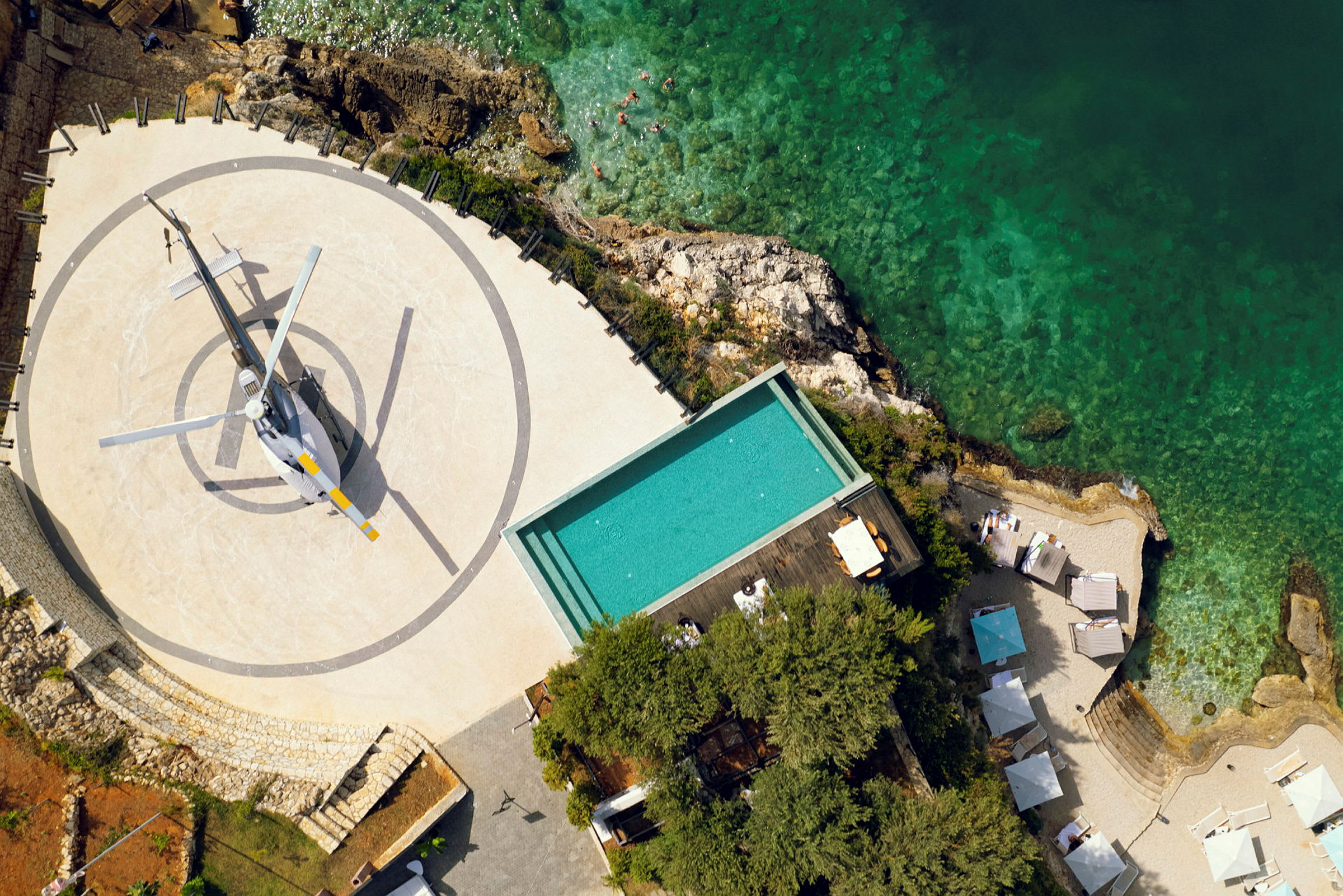 Luftfoto af en helikopter på en landingsplatform nær en pool og kystlinje. (AI-genereret tekst)