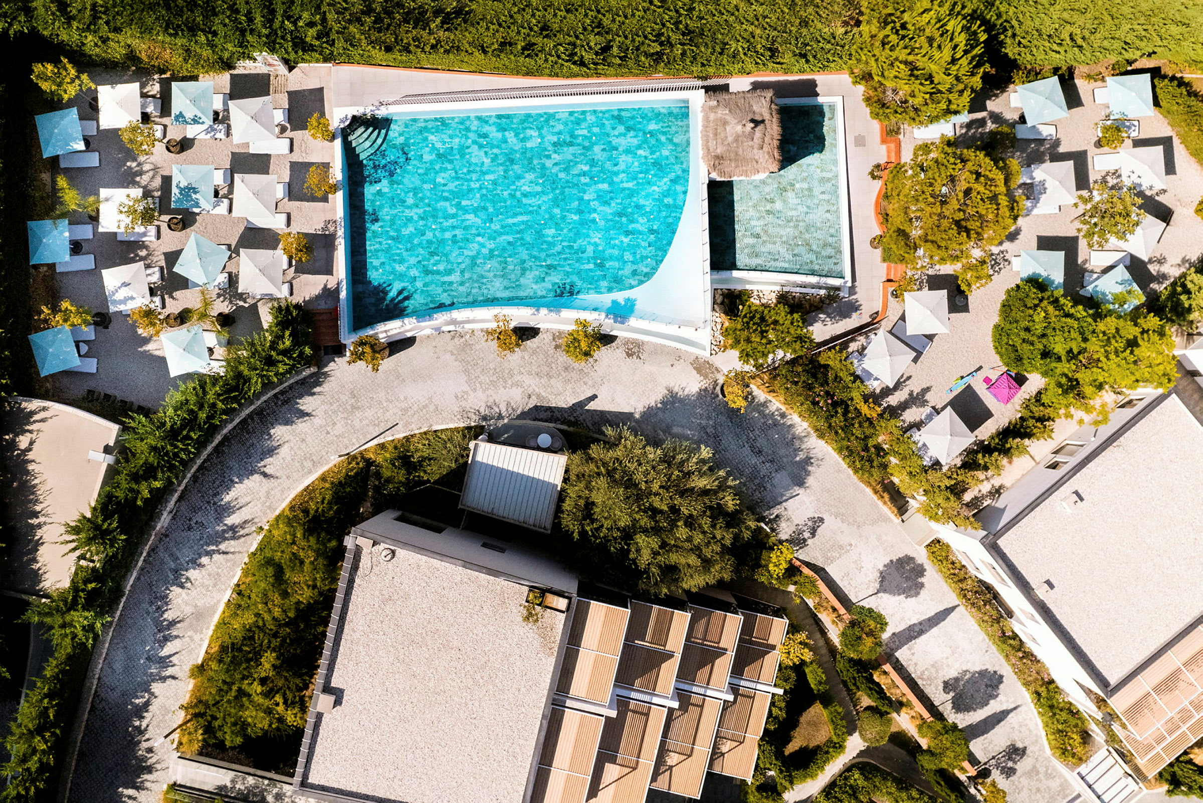 Luftfoto af en pool med omkringliggende liggestole og parasoller. (AI-genereret tekst)