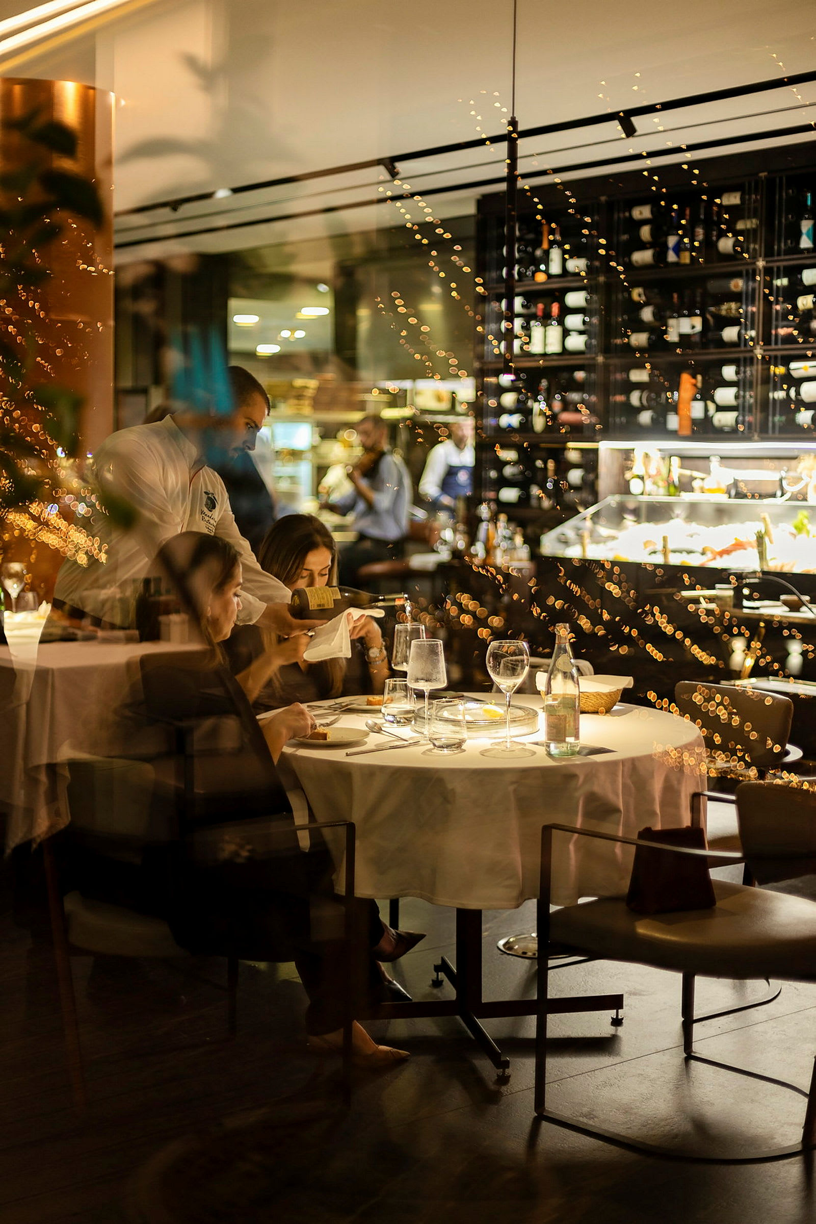 En restaurant med et bord dækket til et måltid og en vinreol i baggrunden. (AI-genereret tekst)