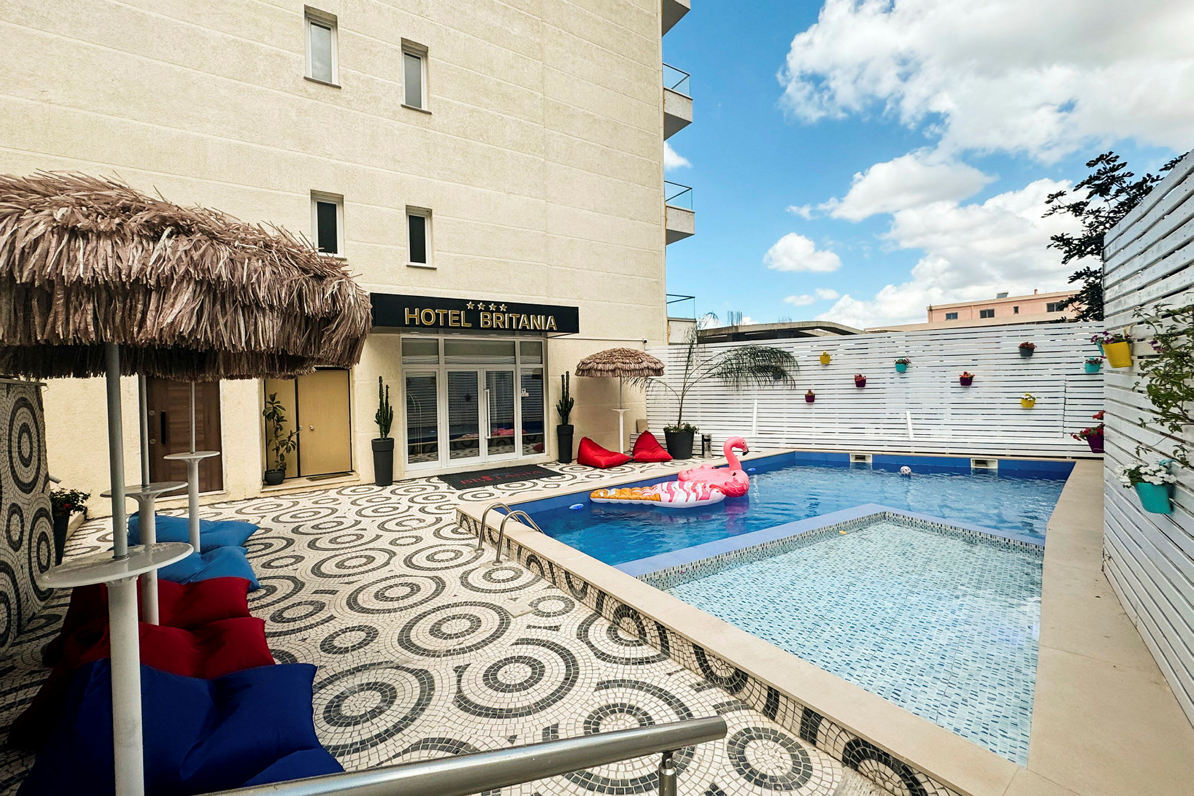 Billede af en hotelpool med oppustelige legetøj og dekorationer, omgivet af en terrasse med farverige møbler og parasoller. (AI-genereret tekst)