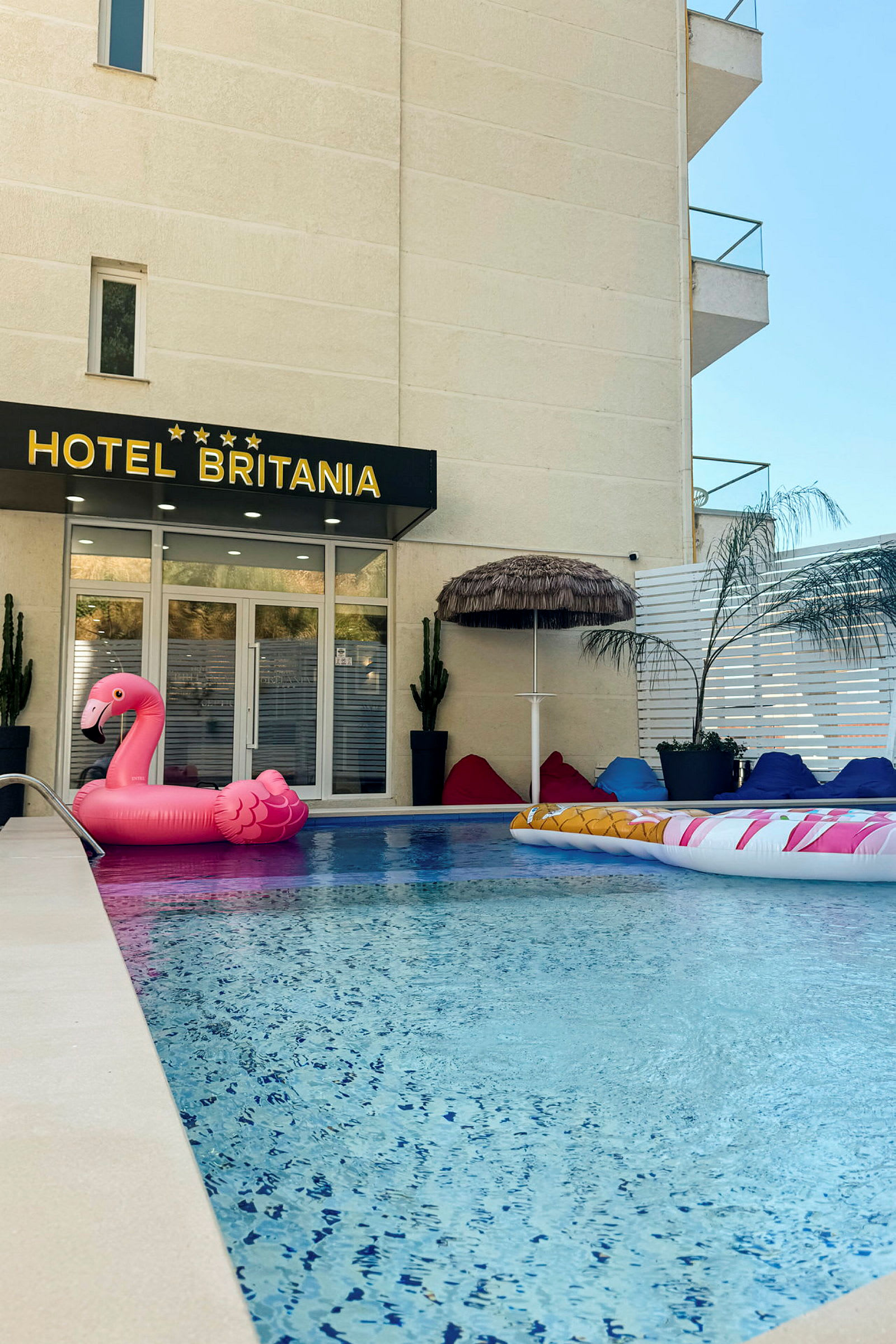 Hotellets poolområde med en lyserød oppustelig flamingo og sækkestole. (AI-genereret tekst)
