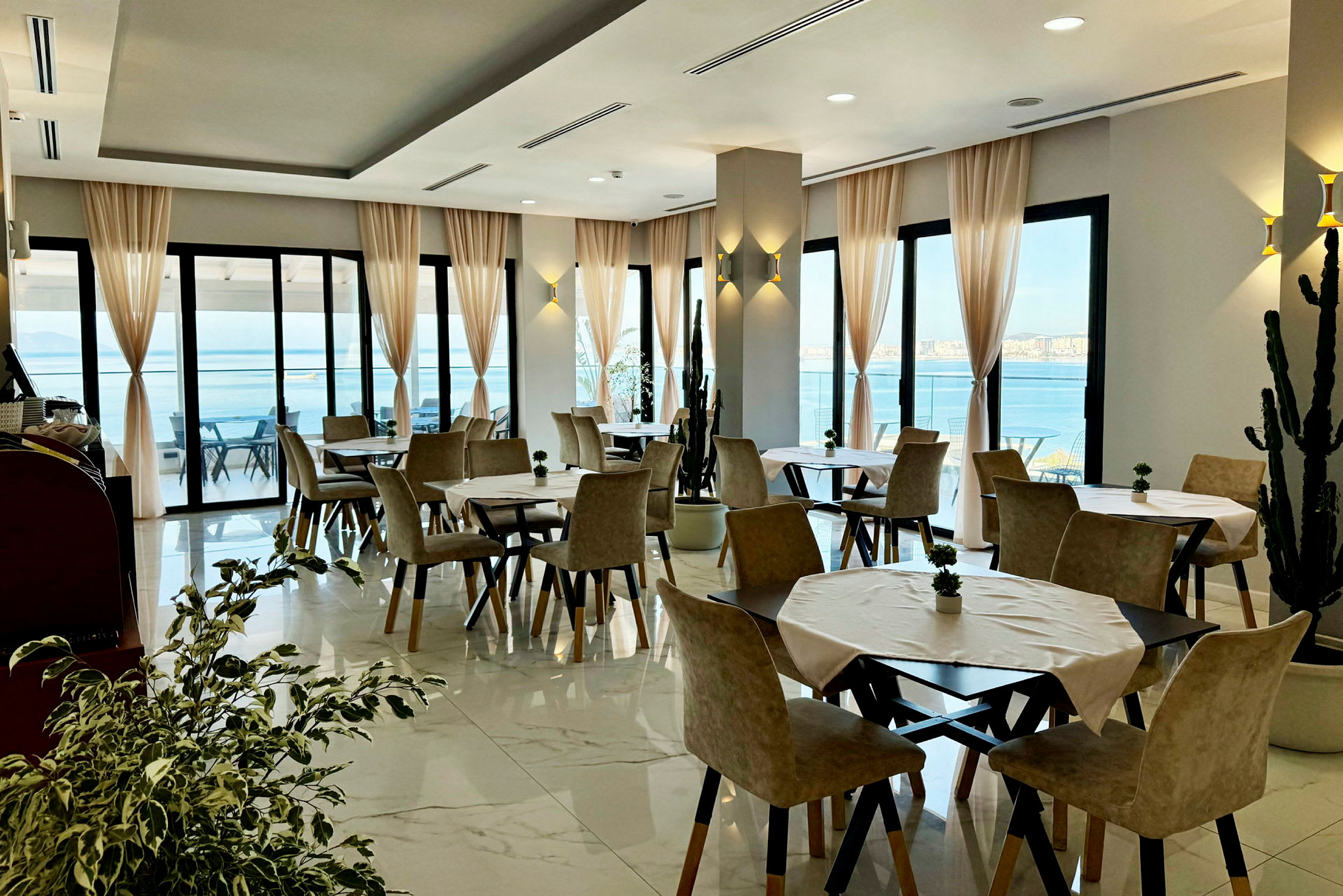 En restaurant med borde og stole samt store vinduer med udsigt over havet. (AI-genereret tekst)