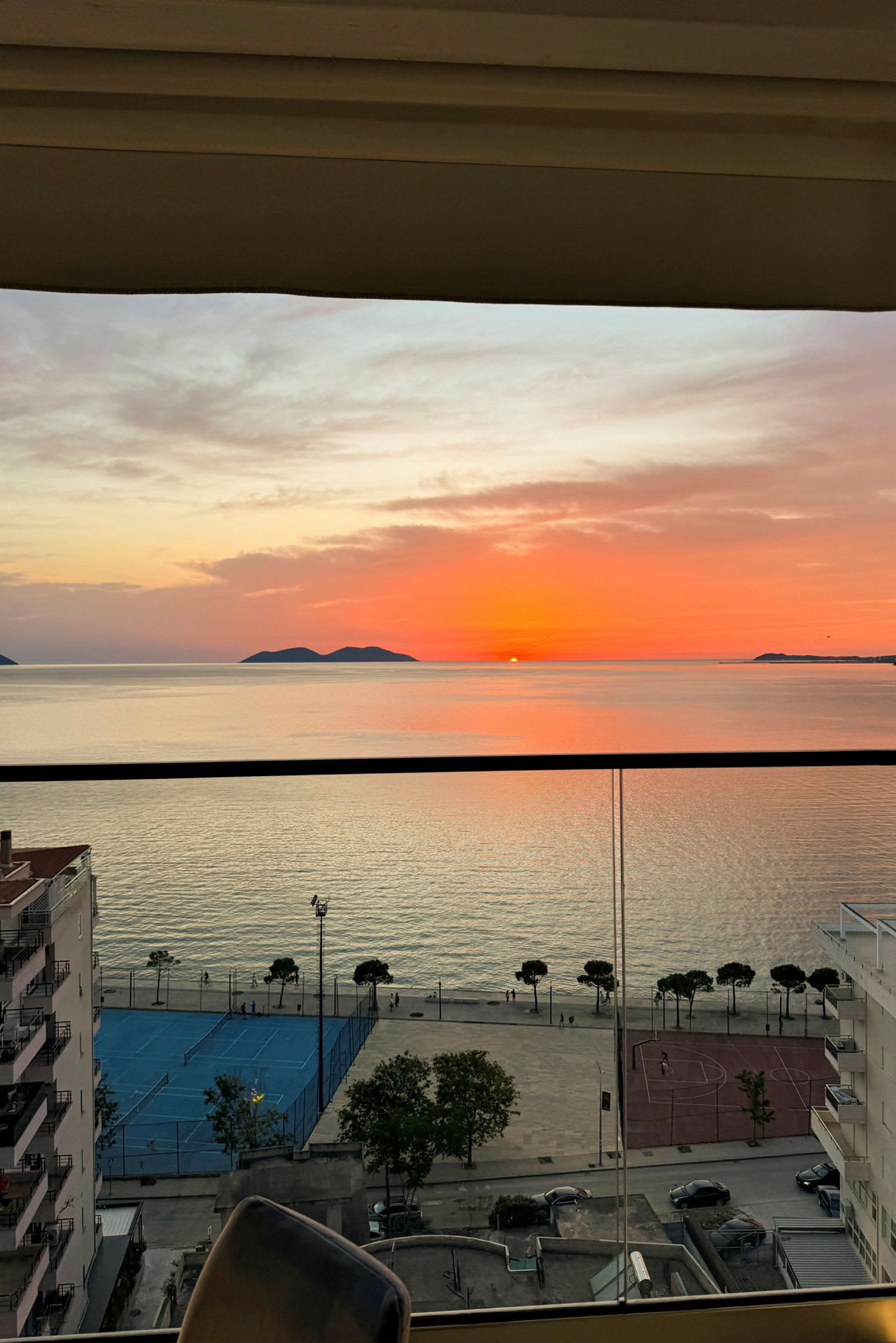 Solnedgang over havet med bygninger og sportsplads i forgrunden. (AI-genereret tekst)