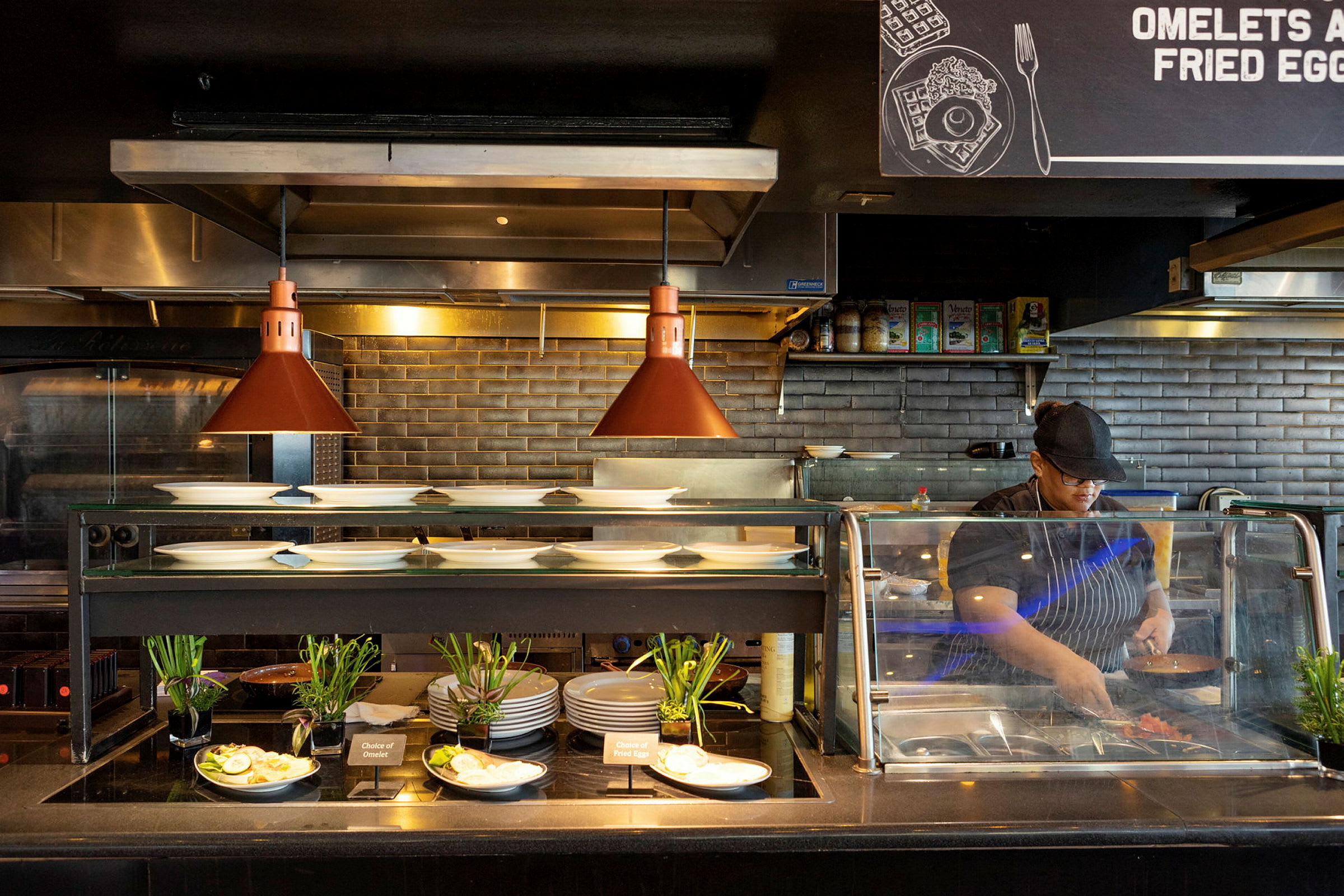 Et restaurantkøkken med tallerkener, tilbehør og en serveringszone oplyst af varmelamper. (AI-genereret tekst)