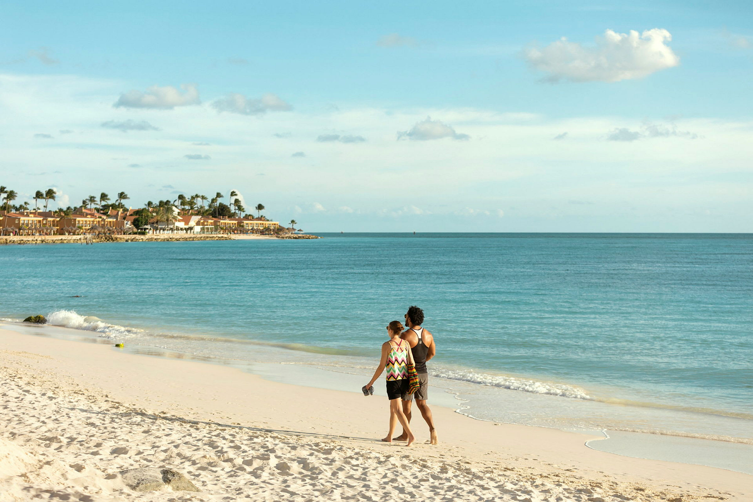 Et par spadserer langs en sandstrand med udsigt over havet og bygningerne langs kysten. (AI-genereret tekst)