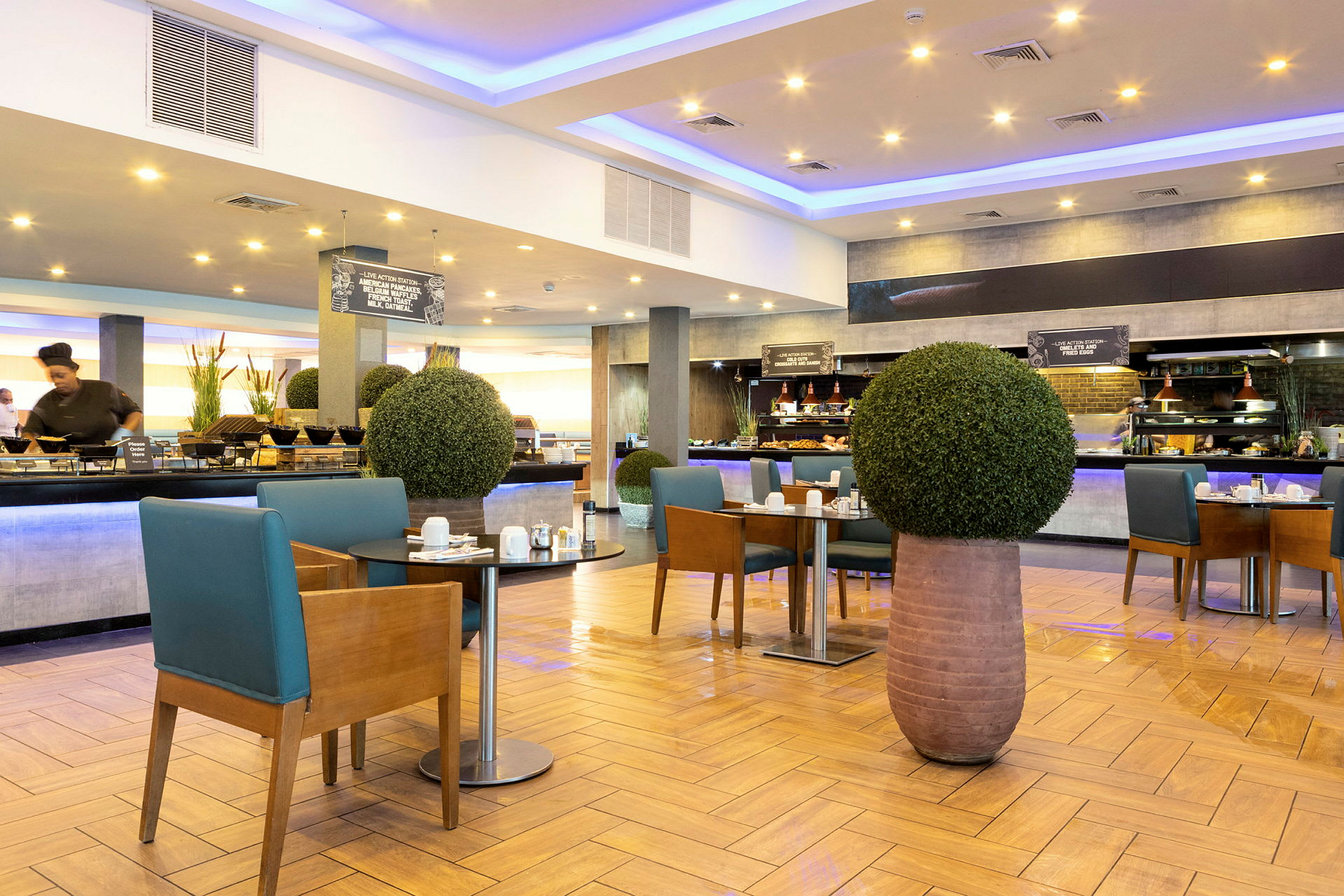 En moderne hotelrestaurant med morgenmadsbuffet og borde dekoreret med grønne planter. (AI-genereret tekst)