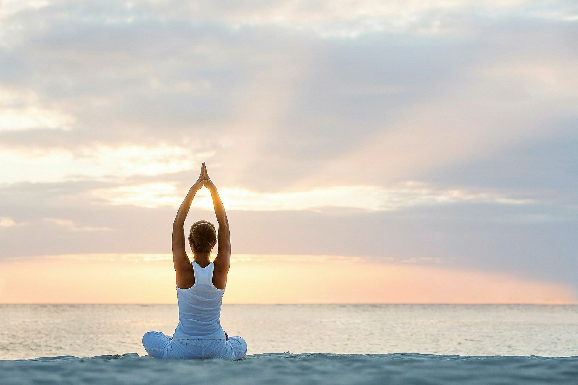 En person sidder på stranden ved solopgang og laver yoga med armene strakt op. (AI-genereret tekst)