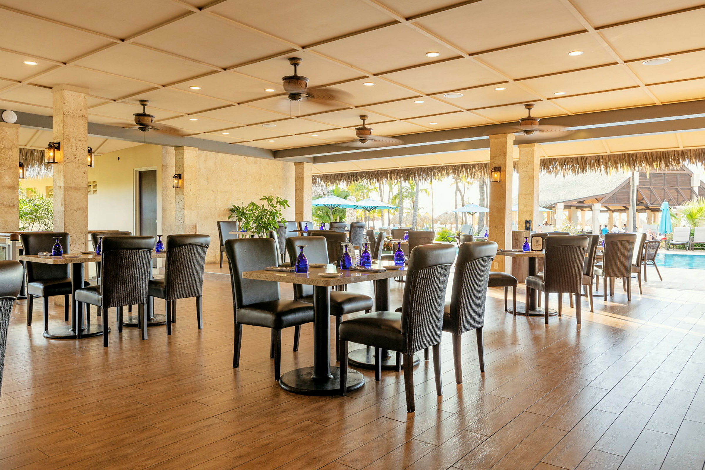 Et luftigt og lyst restaurantområde med borde og stole, og åbning mod en pool og udendørsmiljø. (AI-genereret tekst)
