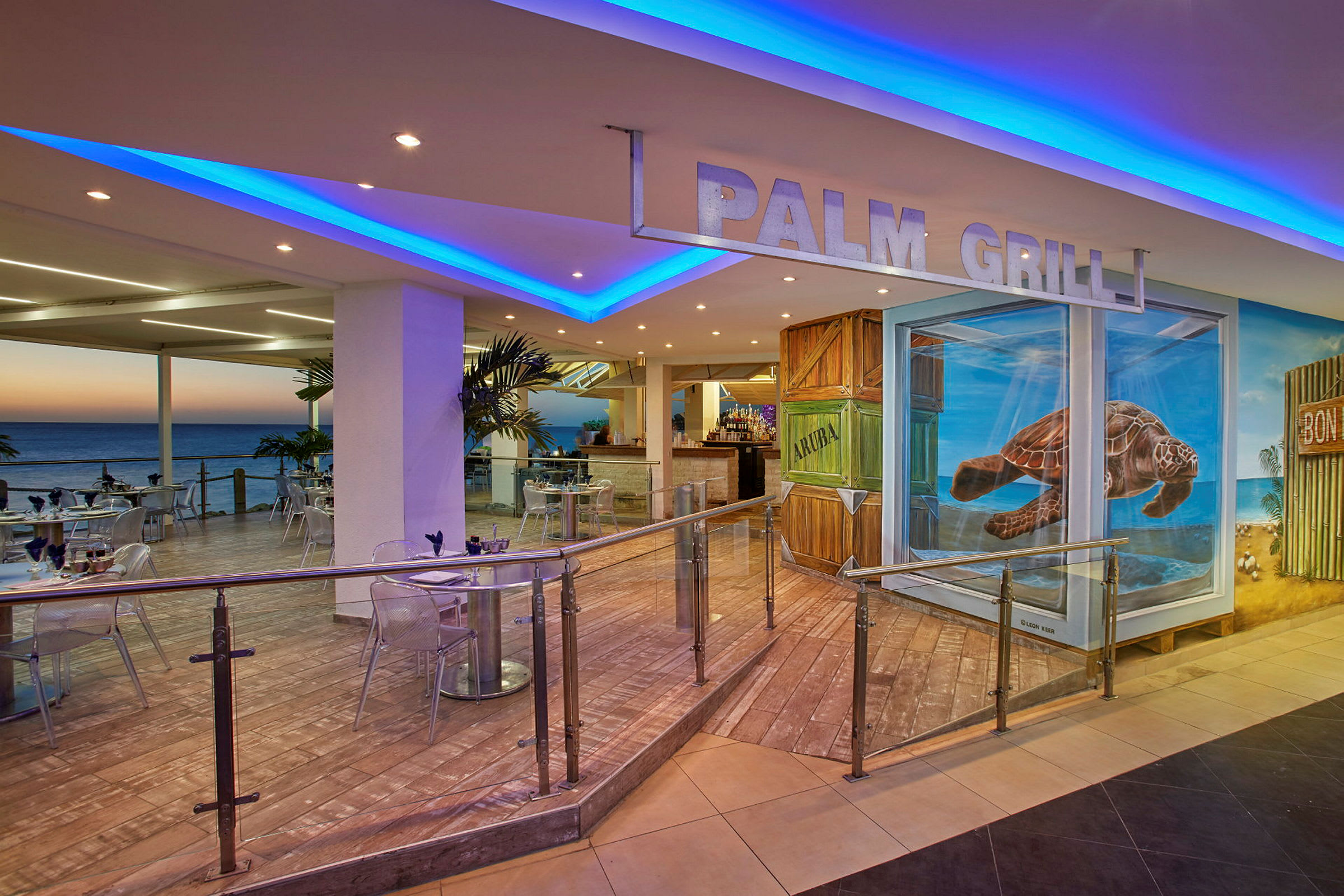 Interiøret af en restaurant med havudsigt, udendørs servering og et skilt med teksten "Palm Grill". Væggene er dekoreret med malerier, herunder en skildpadde. (AI-genereret tekst)