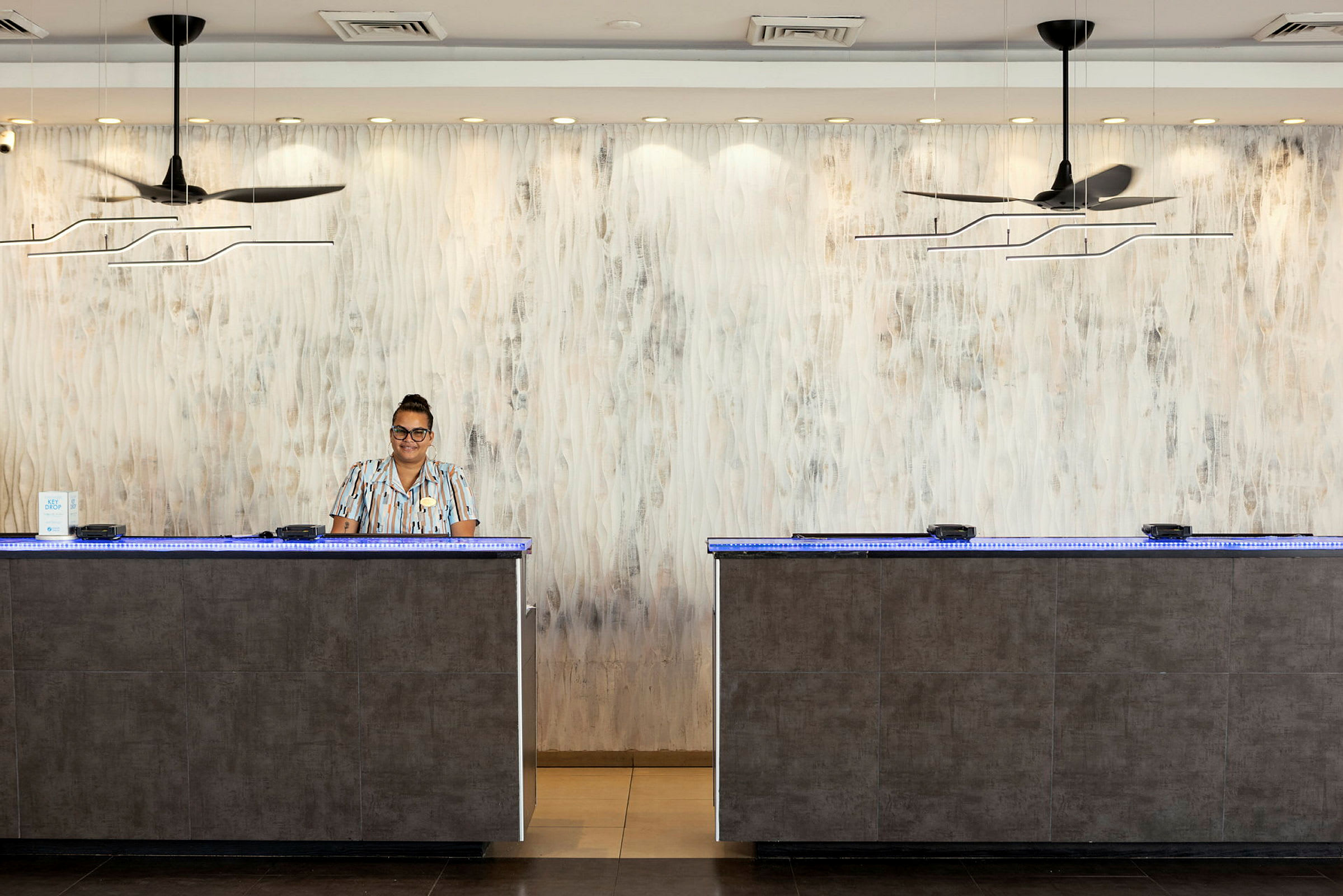 Reception med to skranker på et hotel, dekoreret med moderne lamper og en lys væg. (AI-genereret tekst)
