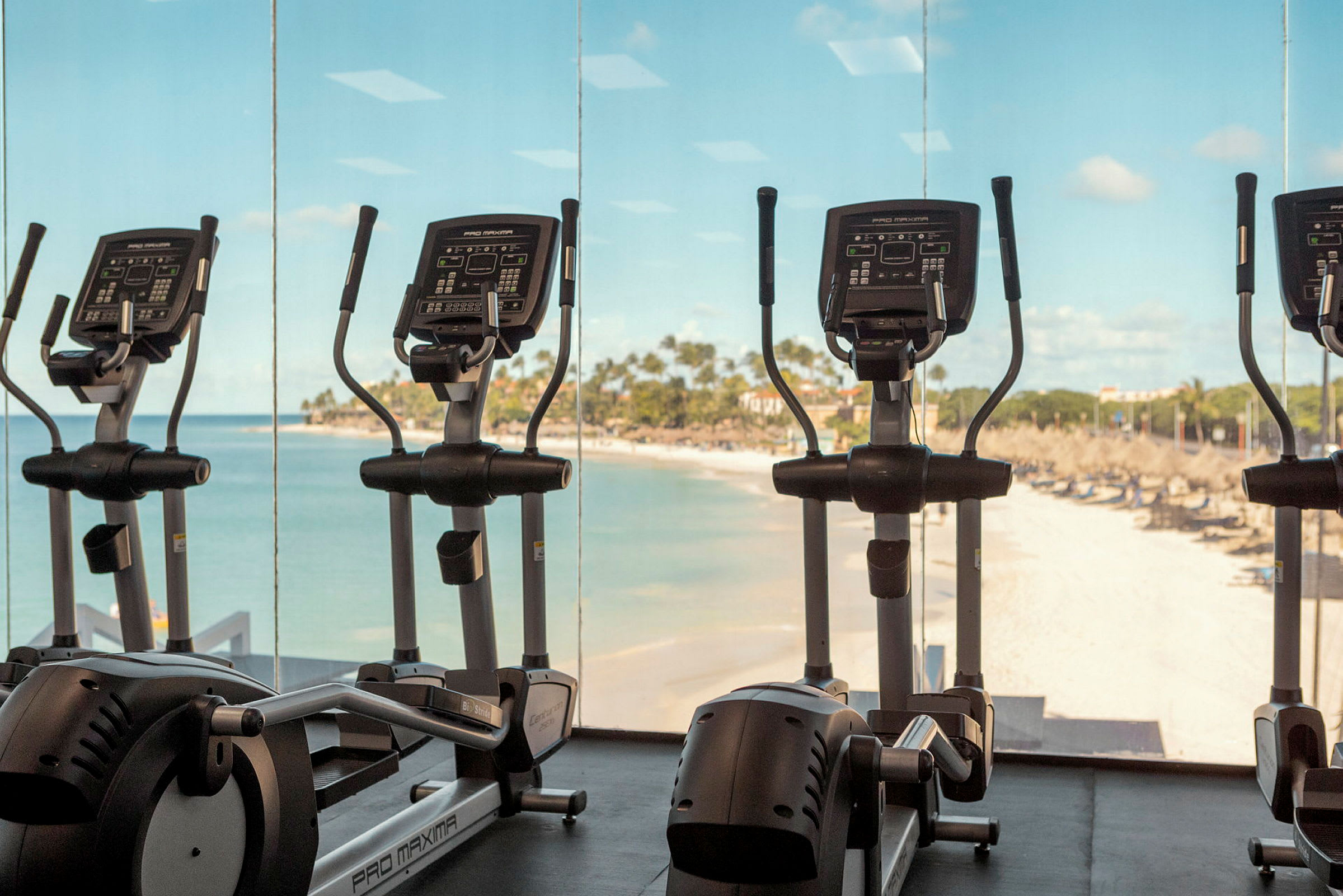 Træningscykler i et fitnesscenter med udsigt til en sandstrand og havet. (AI-genereret tekst)