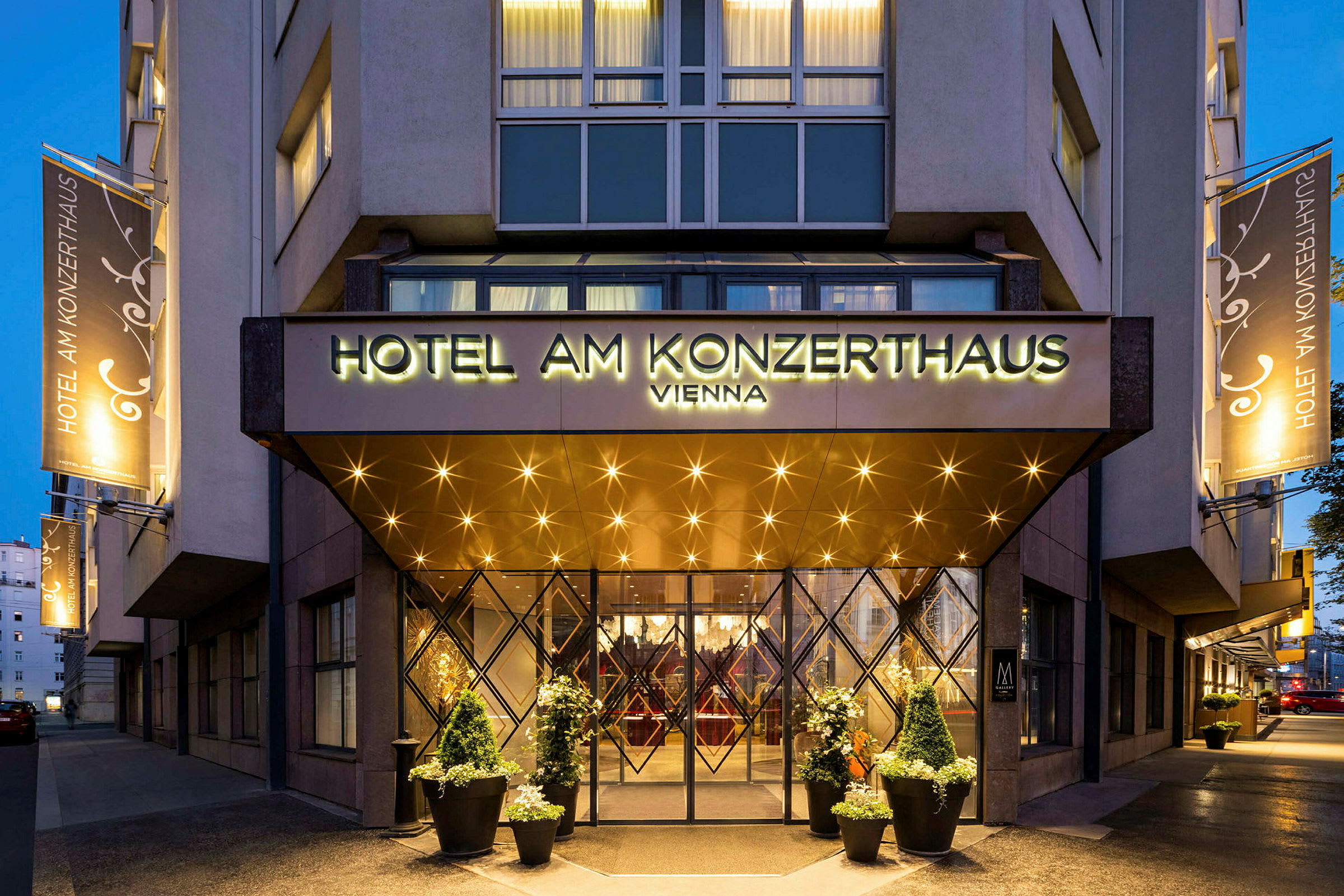 Indgangen til et hotel med et skilt, der lyder "Hotel am Konzerthaus Vienna". Belysning og dekorationer vises omkring indgangen og på facaden. (AI-genereret tekst)