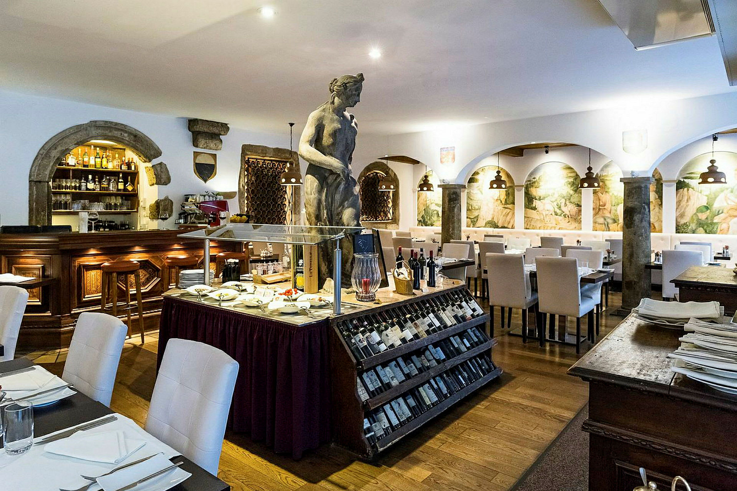 En restaurant med hvidt interiør, en skulptur i midten og en udstilling med vin og delikatesser. (AI-genereret tekst)