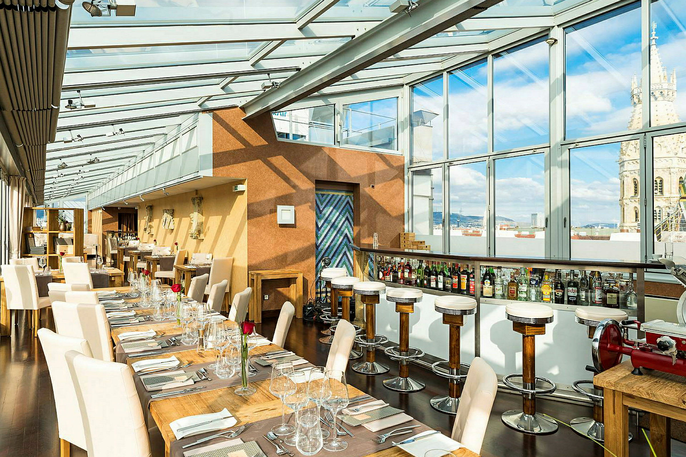 Interiør af en restaurant med glasvægge og -tag, der lader naturligt lys komme ind. Bordene og stolene er elegant arrangeret med duge og glas. (AI-genereret tekst)