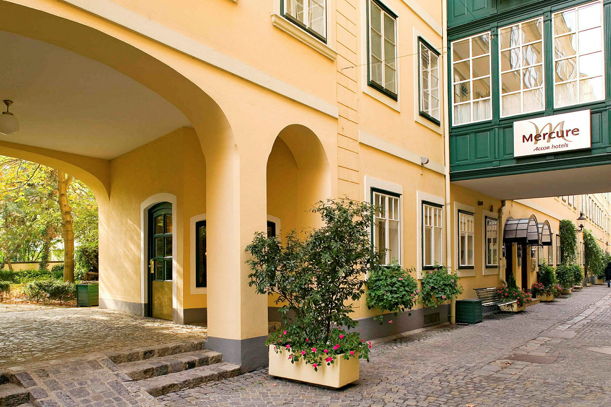 En gård ved hotel Mercure med gule vægge og grønne vinduesrammer, dekoreret med blomster og grøn vegetation. (AI-genereret tekst)