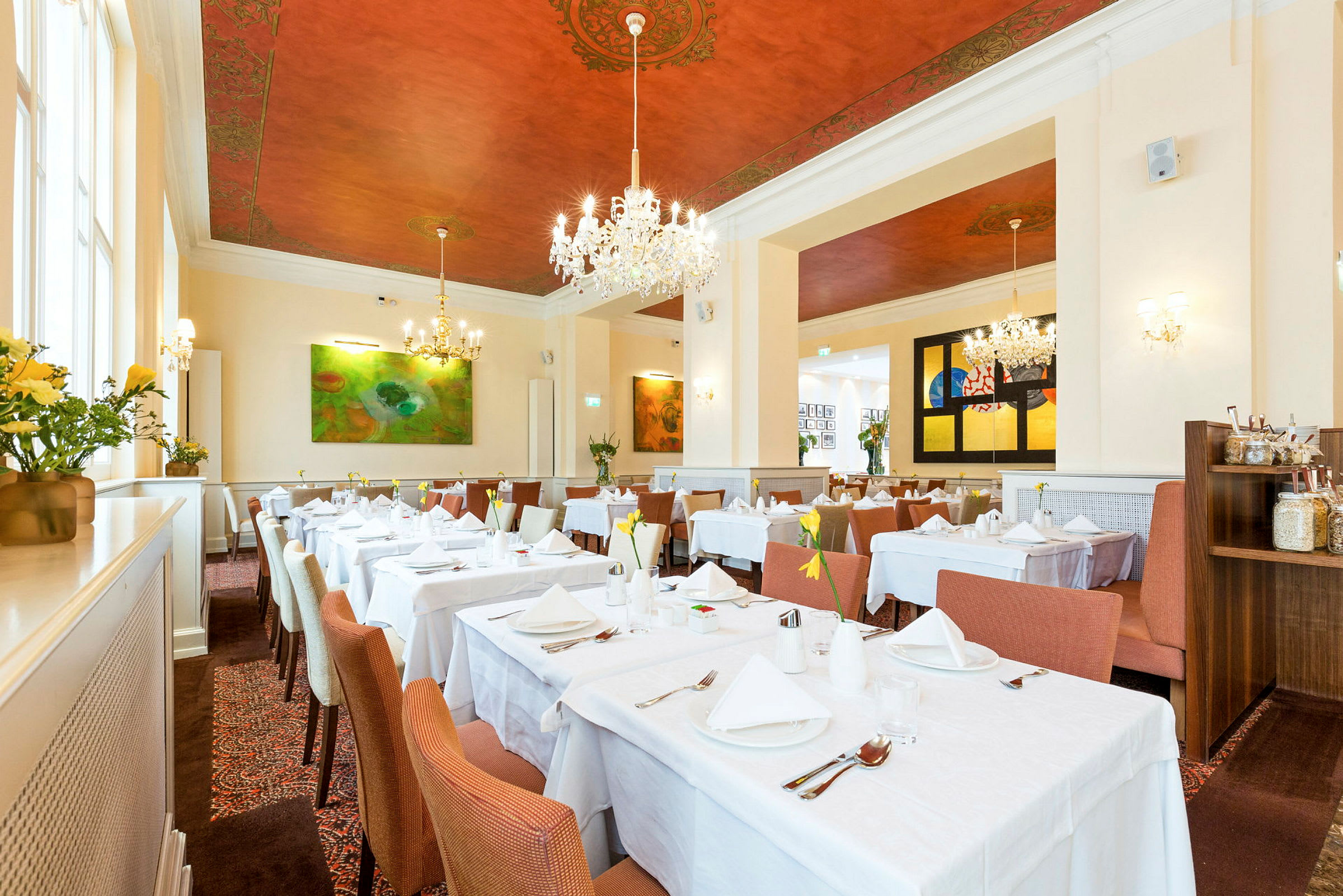 Interiør af en elegant restaurant med hvide duge på bordene, stilfulde stole og dekorativt malet loft. (AI-genereret tekst)