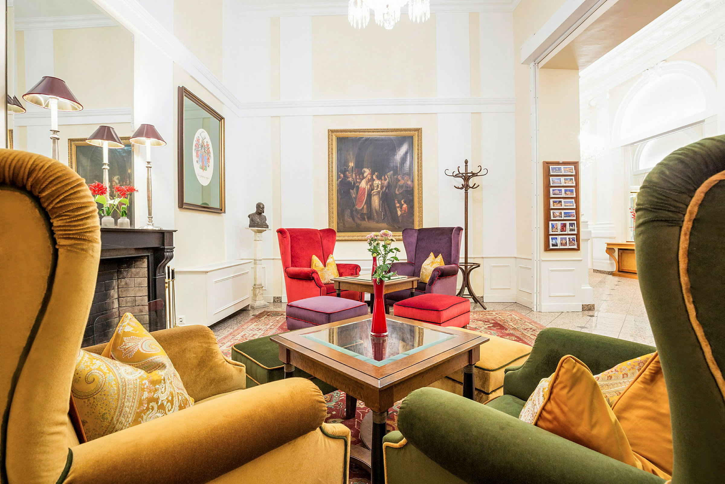 En stilfuldt indrettet lounge med farverige lænestole og sofaer omkring et bord. Væggene er dekoreret med kunst, og en pejs med pynt ses på siden. (AI-genereret tekst)