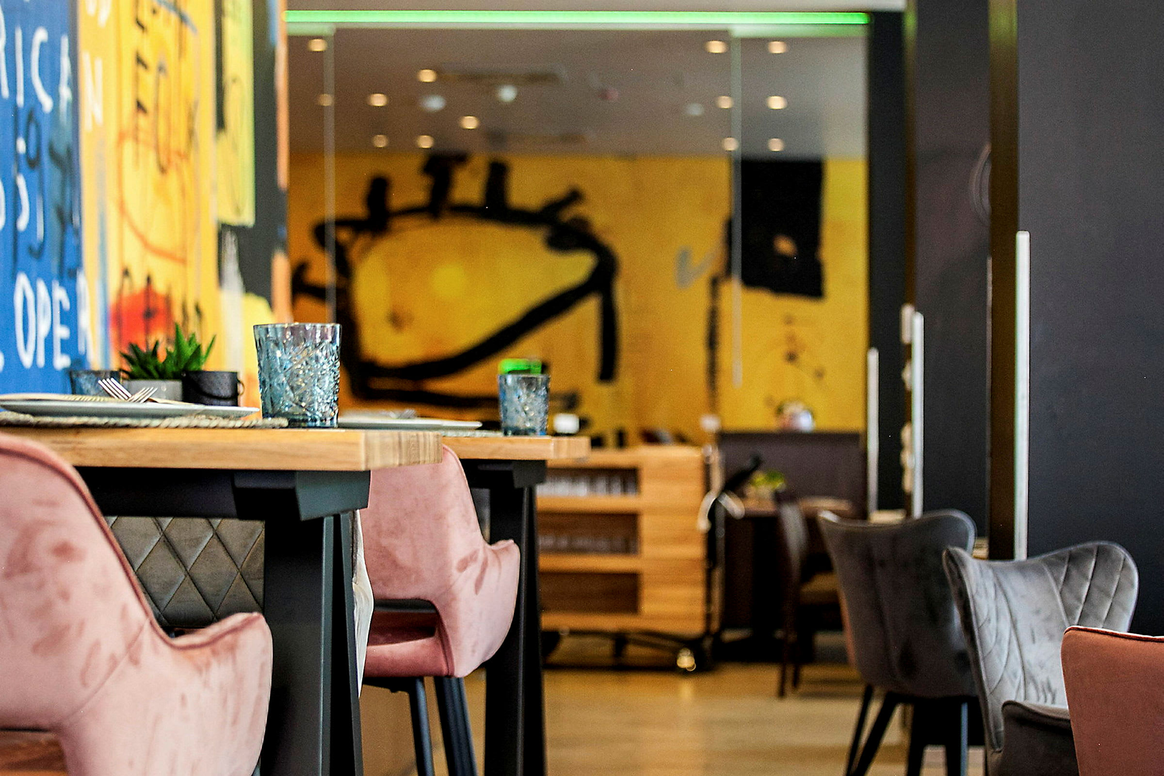 Interiør af en moderne restaurant med farverige vægmalerier og borde med behagelige stole. (AI-genereret tekst)