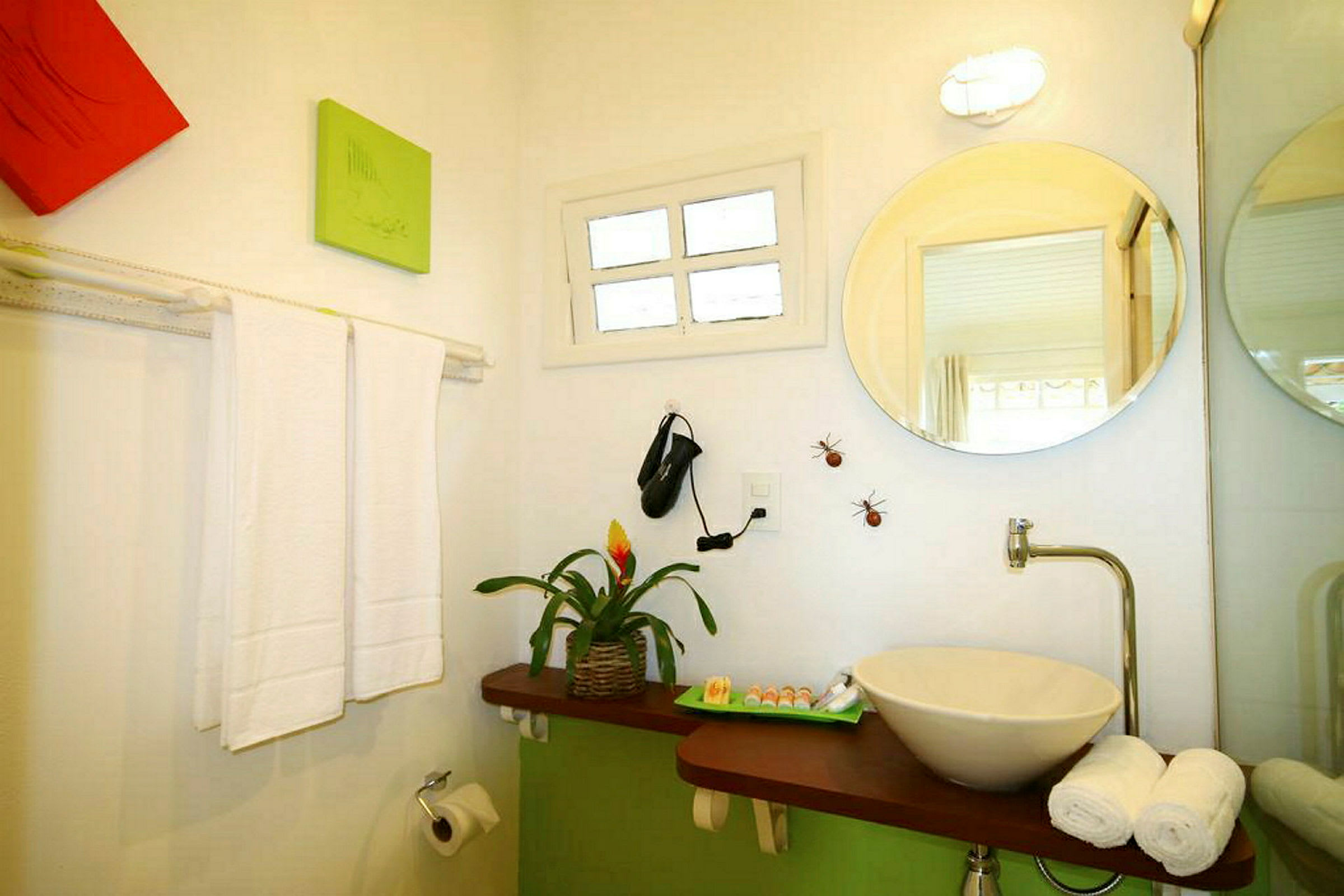 Et badeværelse med håndvask og spejl, dekoreret med planter og pynt. Håndklæder og toiletpapir er synlige. (AI-genereret tekst)
