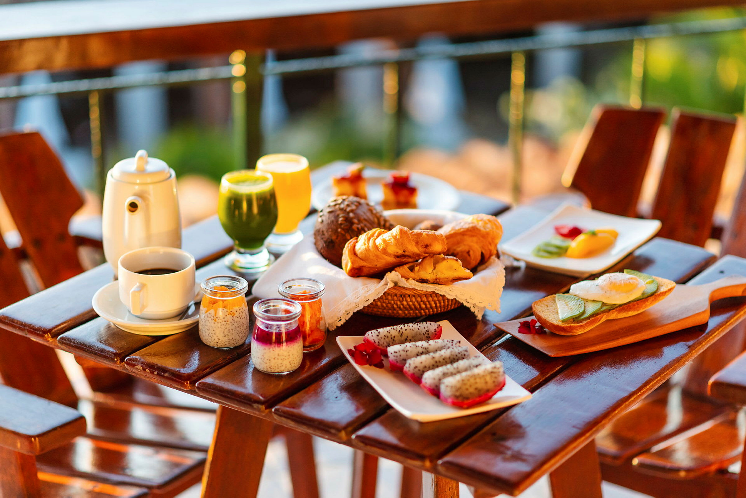 En morgenmad med forskellige retter serveret på et bord udendørs, inklusive brød, croissanter, frisk frugt, juice og kaffe. (AI-genereret tekst)