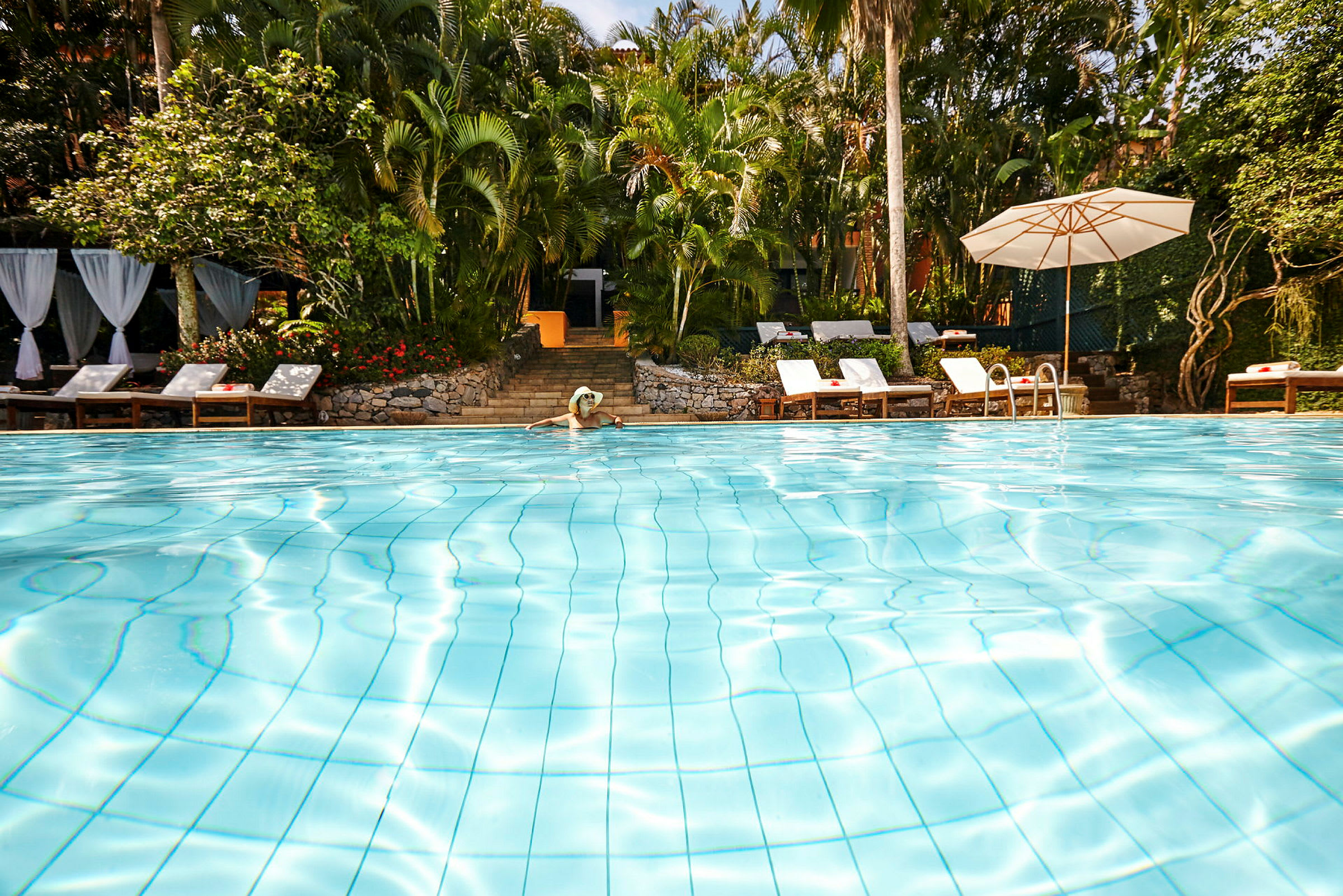 En udendørs swimmingpool omgivet af frodig vegetation og liggestole. (AI-genereret tekst)