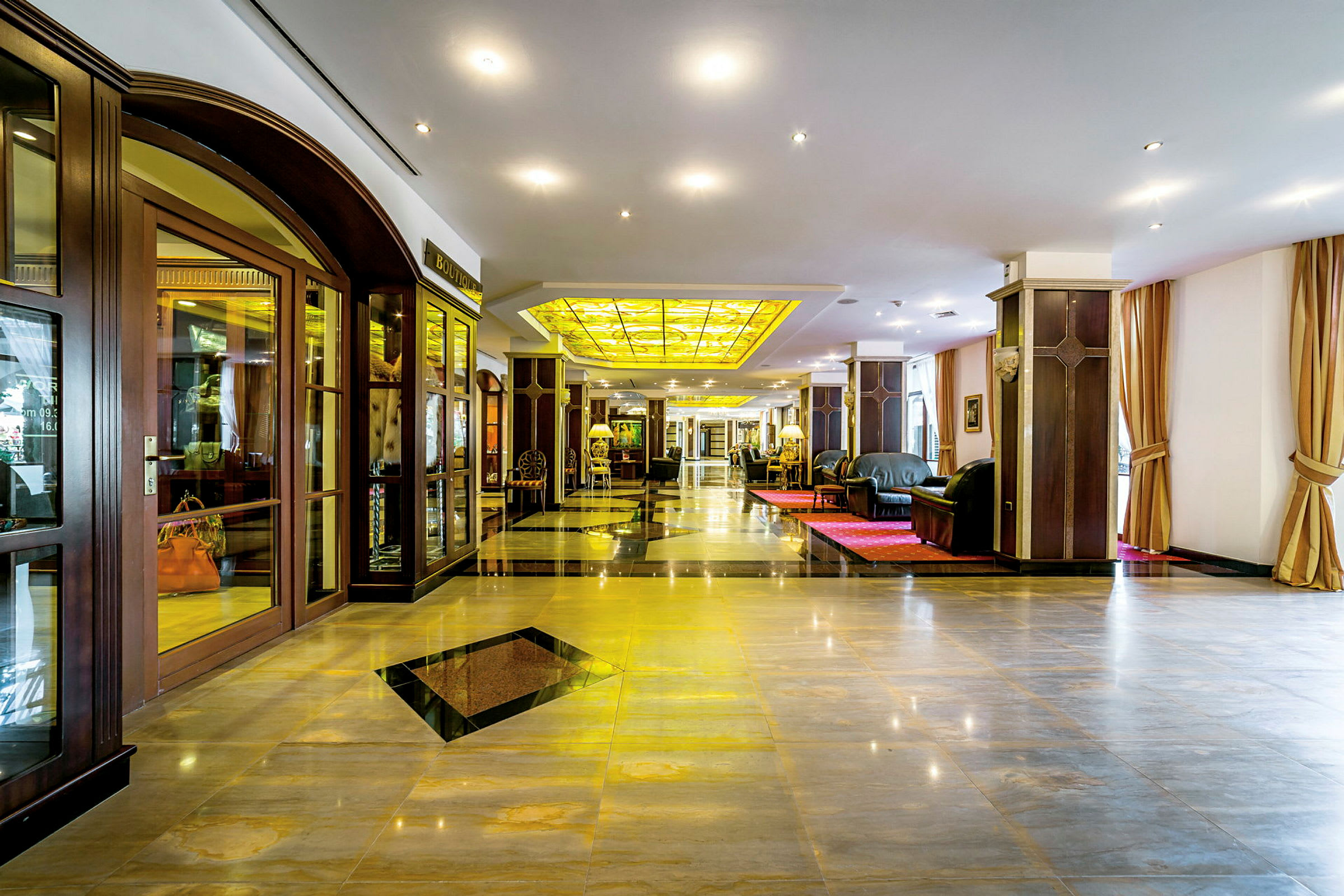 En elegant hotellobby med skinnende gulve, komfortable sofaer og et gult glastag. (AI-genereret tekst)