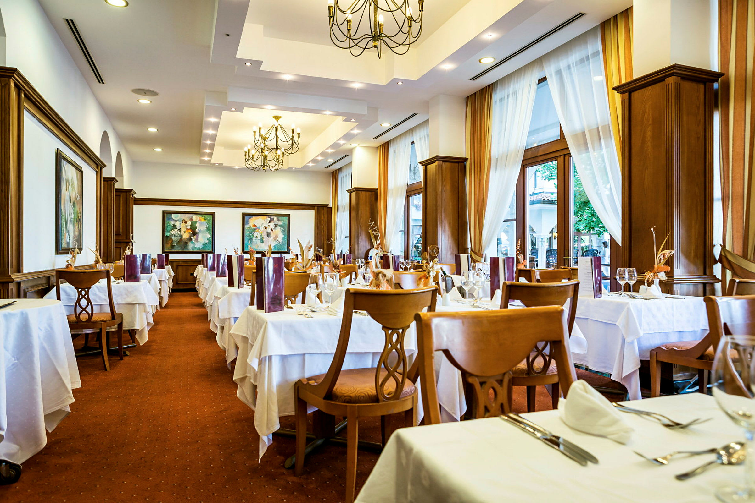 Interiør af en restaurant med dækkede borde og stole, lyse gardiner og dekorative loftlamper. (AI-genereret tekst)