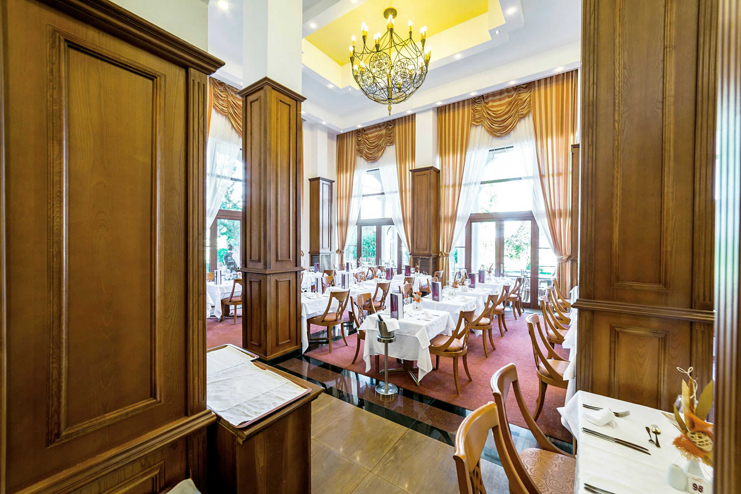 En elegant restaurant med dækkede borde, træpaneler og store vinduer med gardiner. (AI-genereret tekst)
